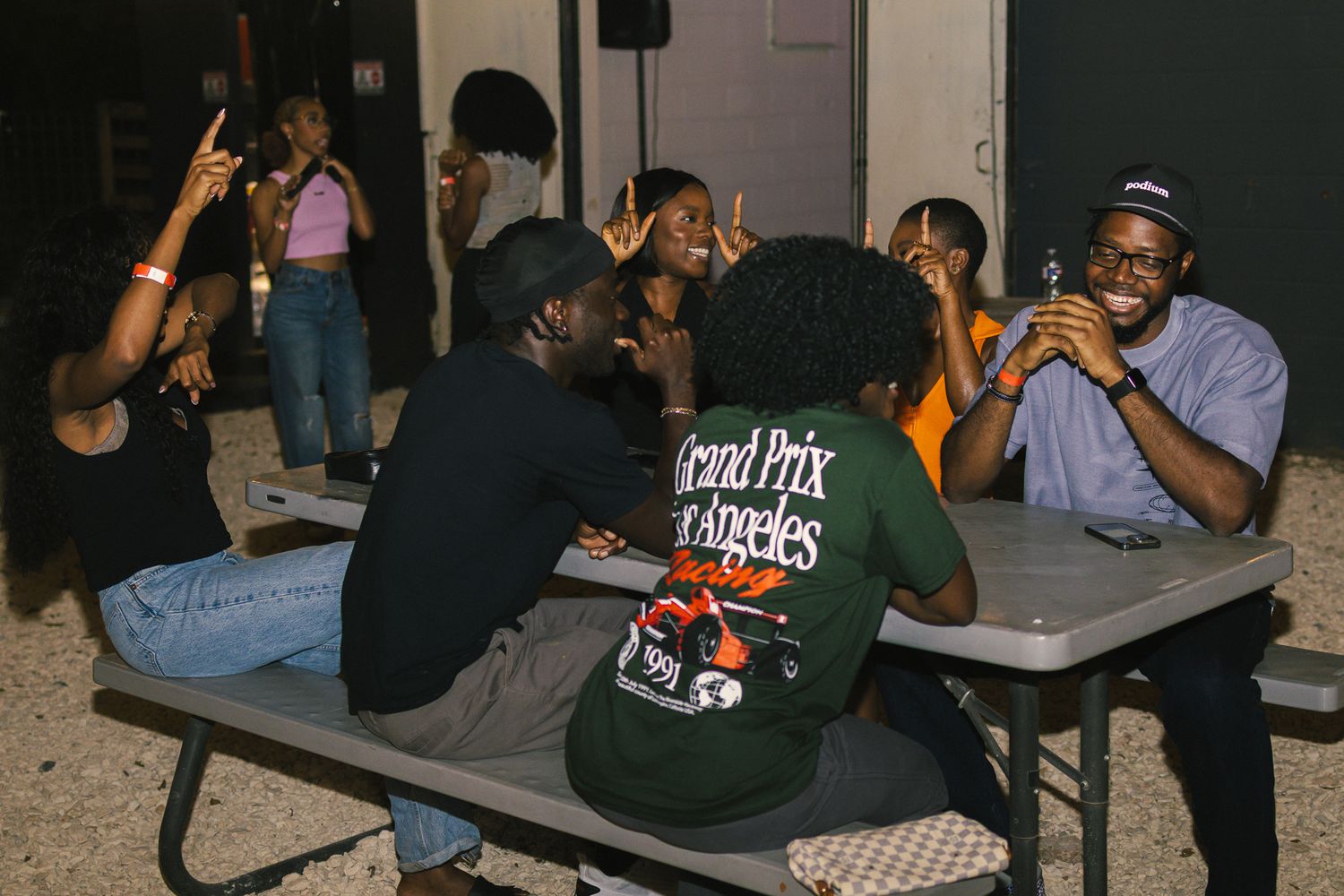 Group socializing at outdoor tables during evening event with string lights overhead.