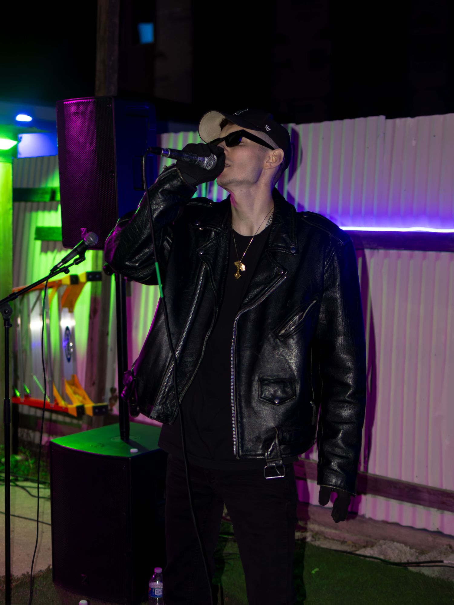 Singer in dark attire performing on stage with colorful lighting effects.
