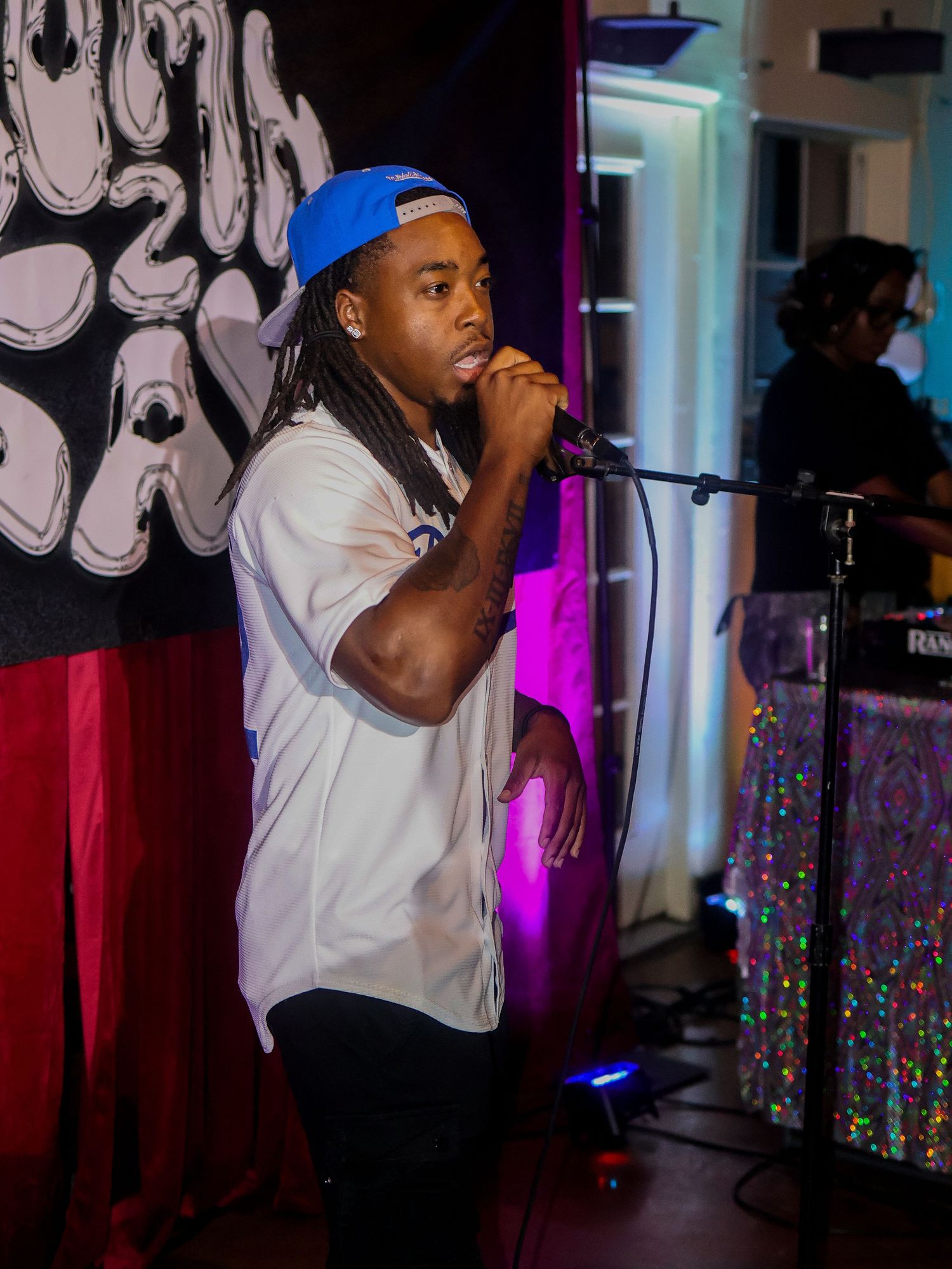 Performer in white shirt and blue cap performing on stage with artistic backdrop.