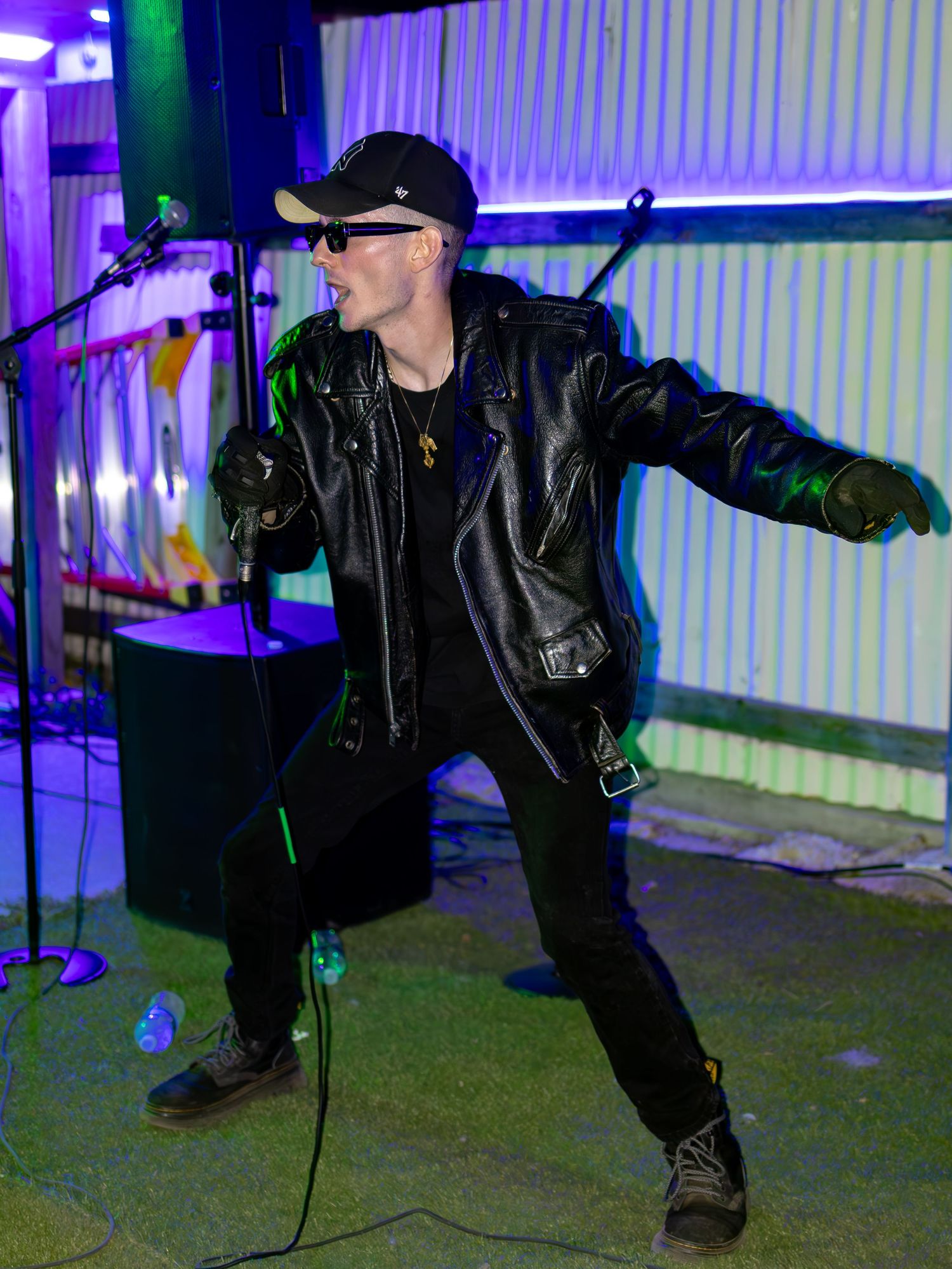 Energetic performer in black attire strikes dramatic pose during stage show with purple backlighting.