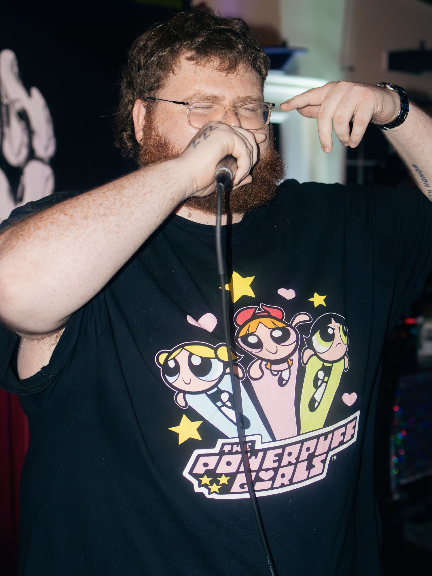 Performer wearing glasses and a black t-shirt with cartoon characters singing into a microphone.
