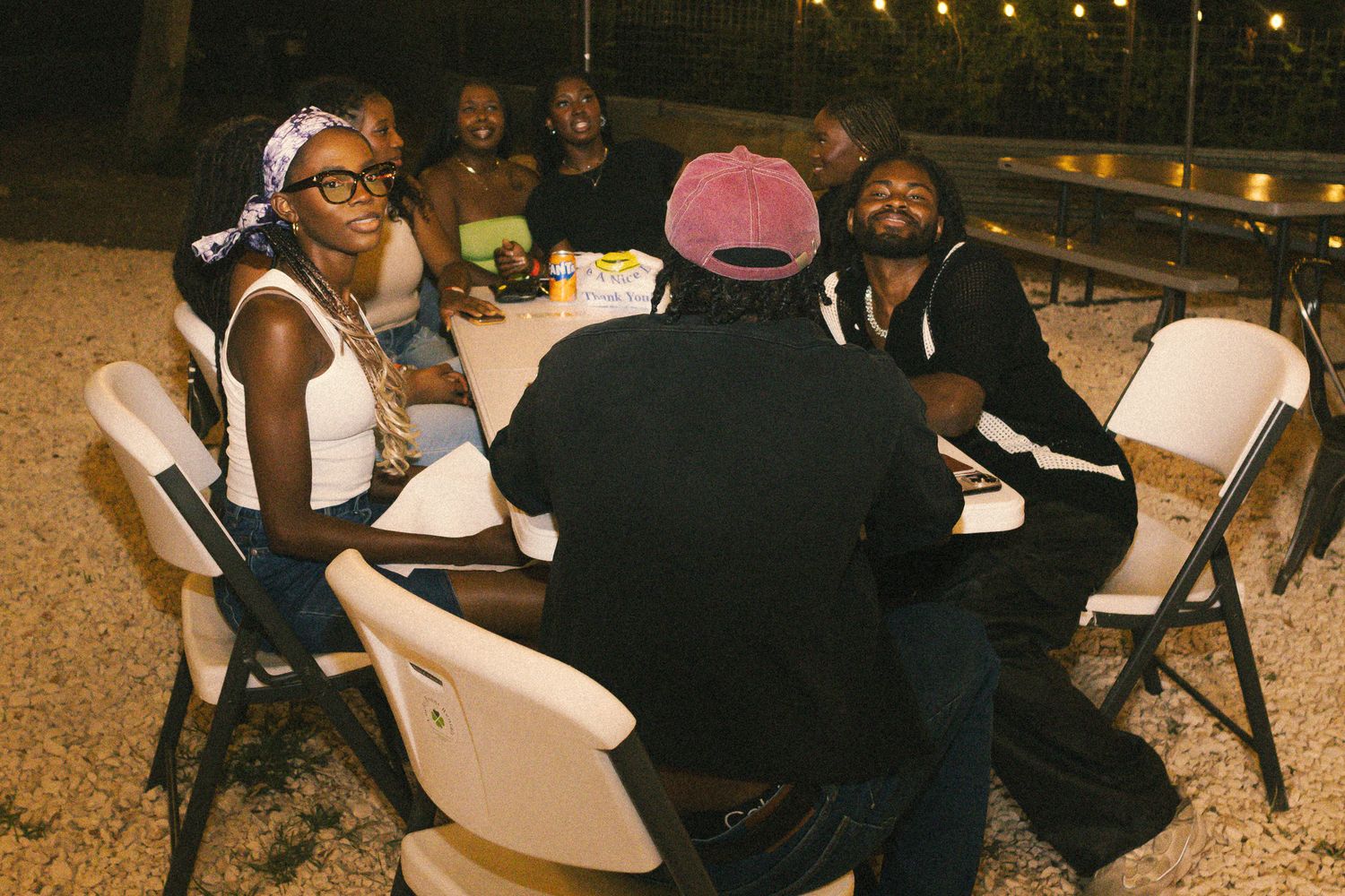 People gathered at tables under string lights for an outdoor nighttime event.