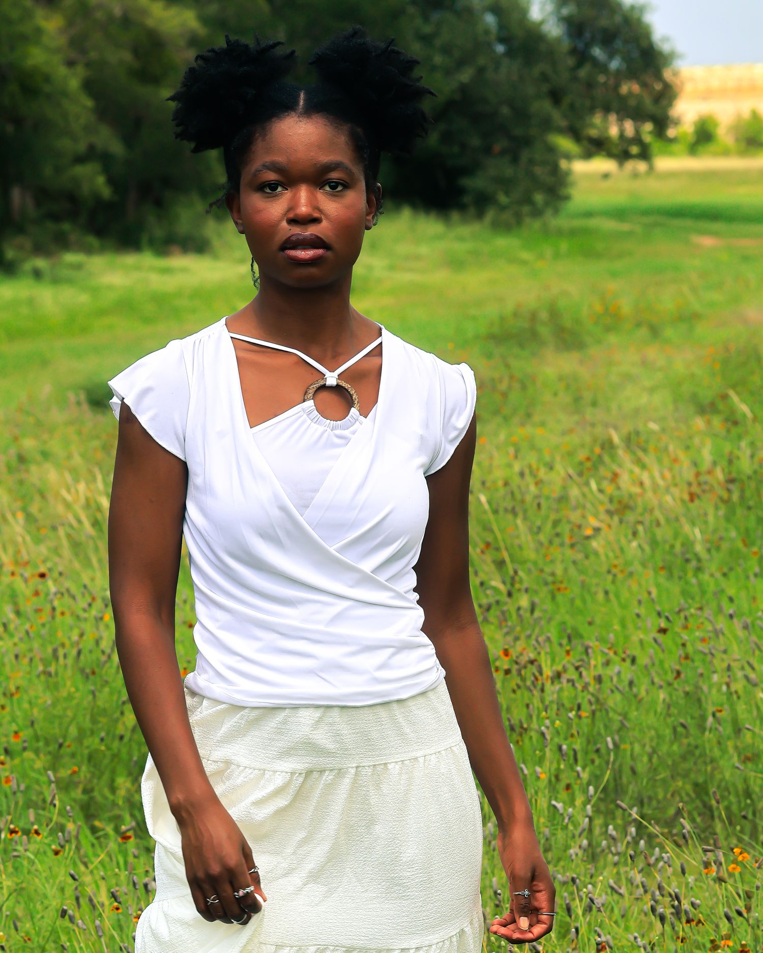 Standing portrait in white outfit against lush green summer background.
