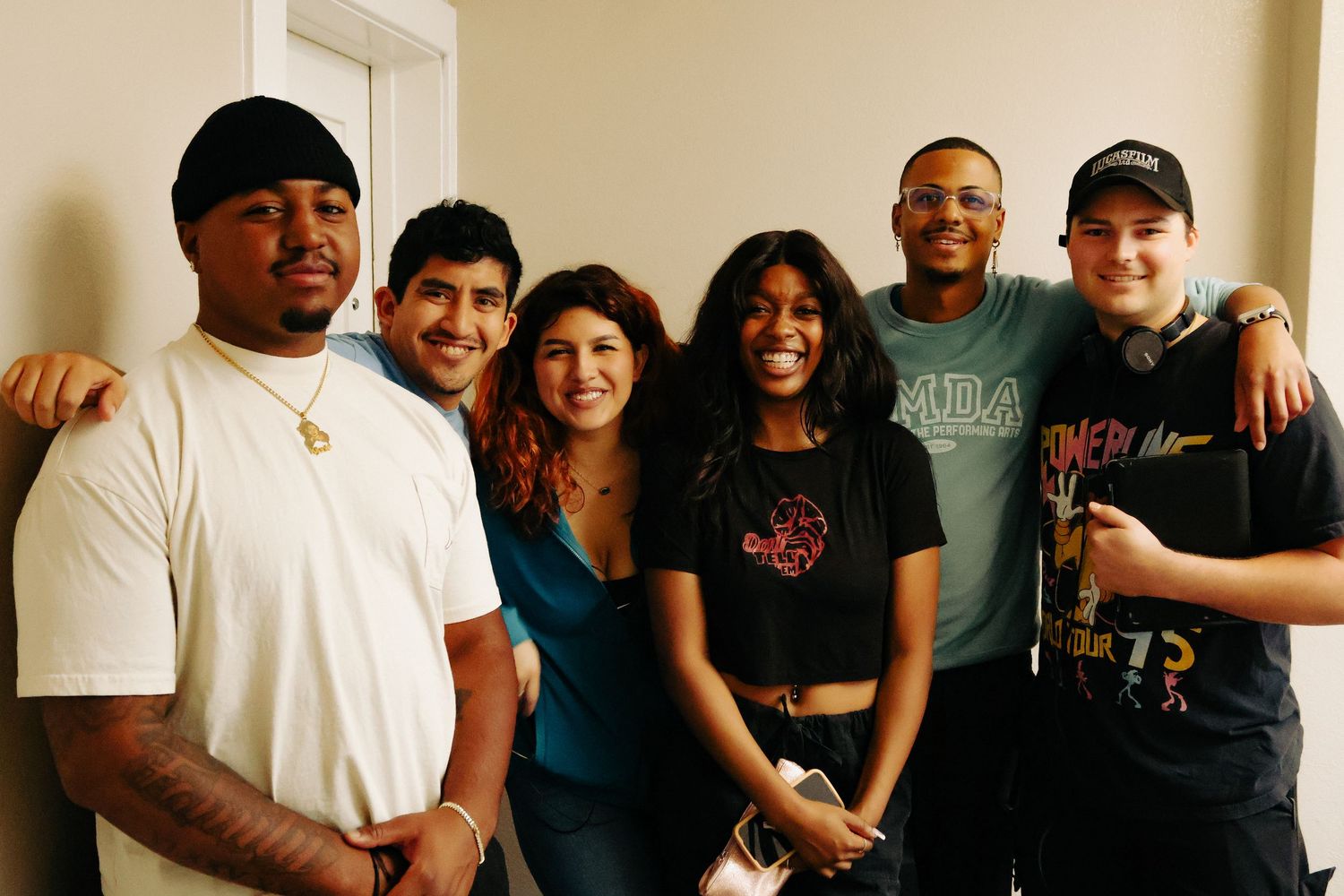 Group of people posing together in a casual indoor setting with light colored walls.