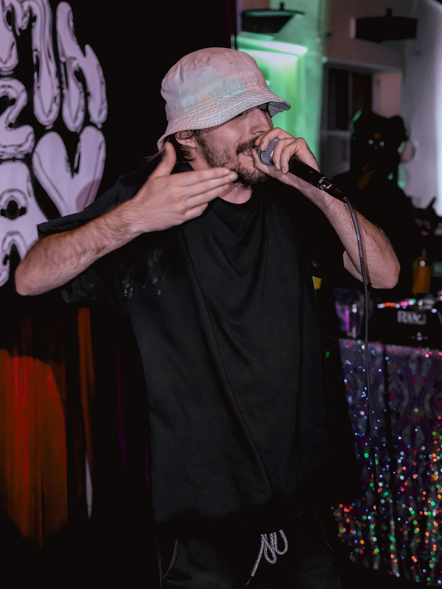Singer in casual attire performing with microphone against illuminated backdrop.