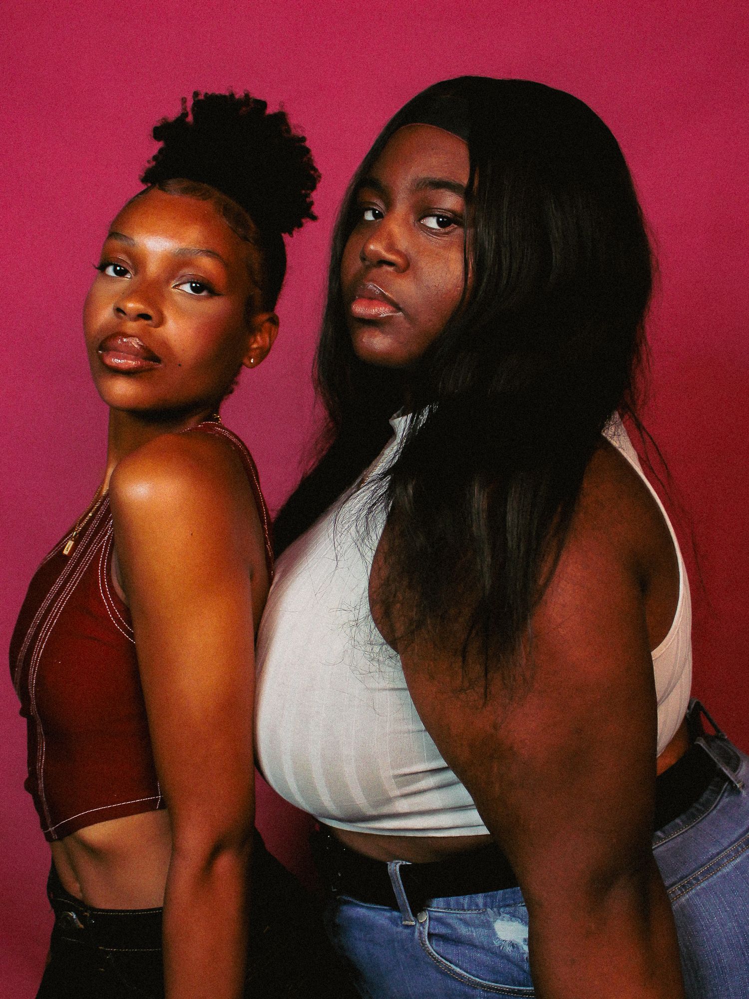 Fashion portrait of two models in casual wear against bright red backdrop.