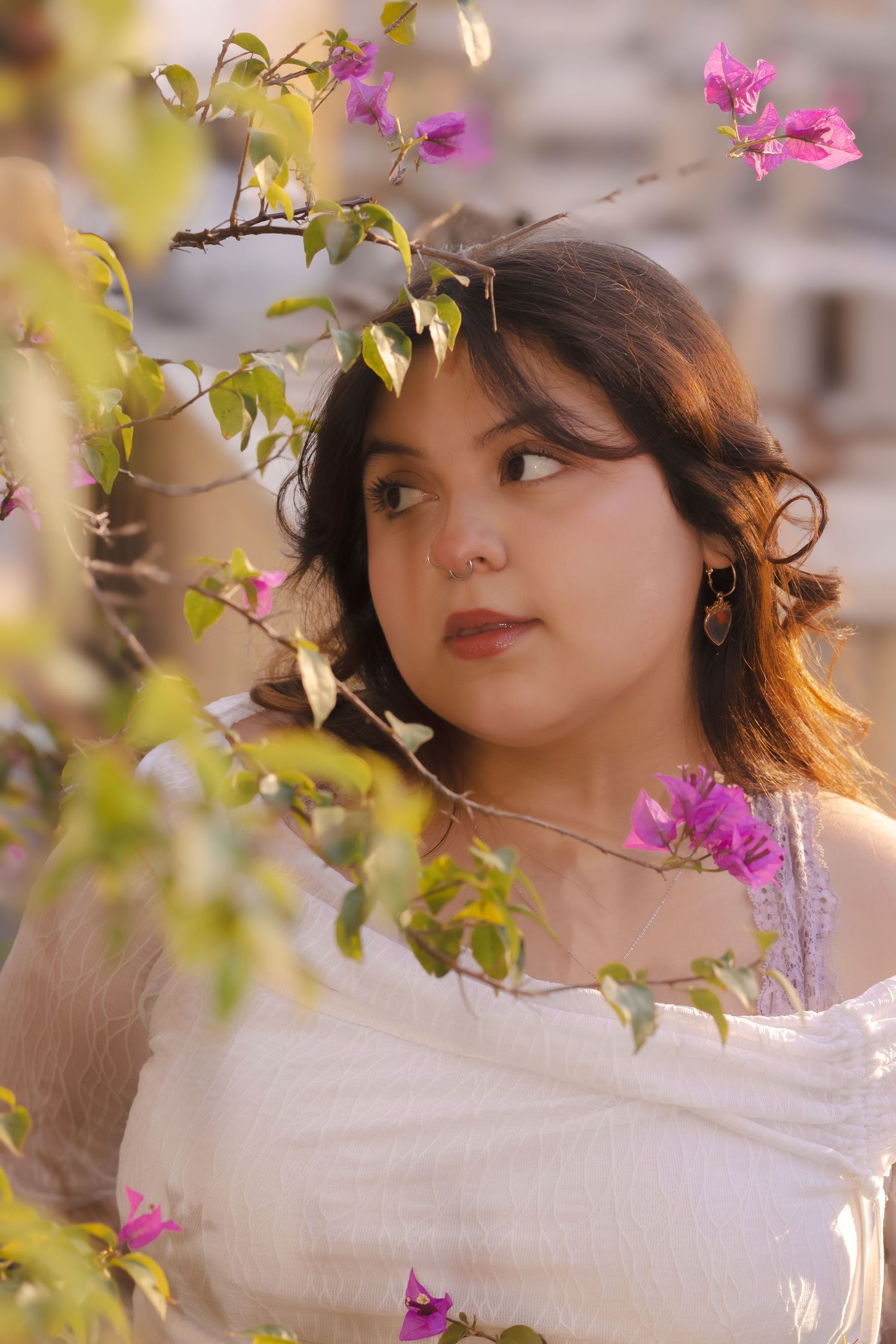Ethereal portrait among pink flowers and greenery wearing a white flowing top.