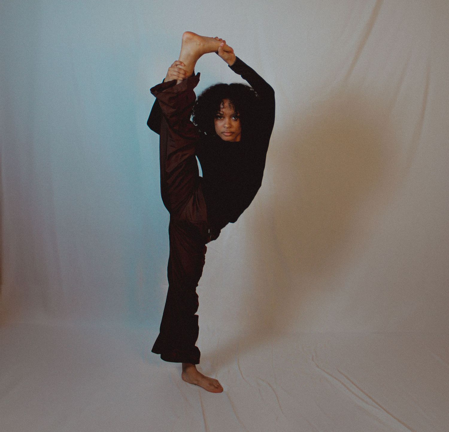 Dancer demonstrates flowing movements in brown attire against white studio setting.