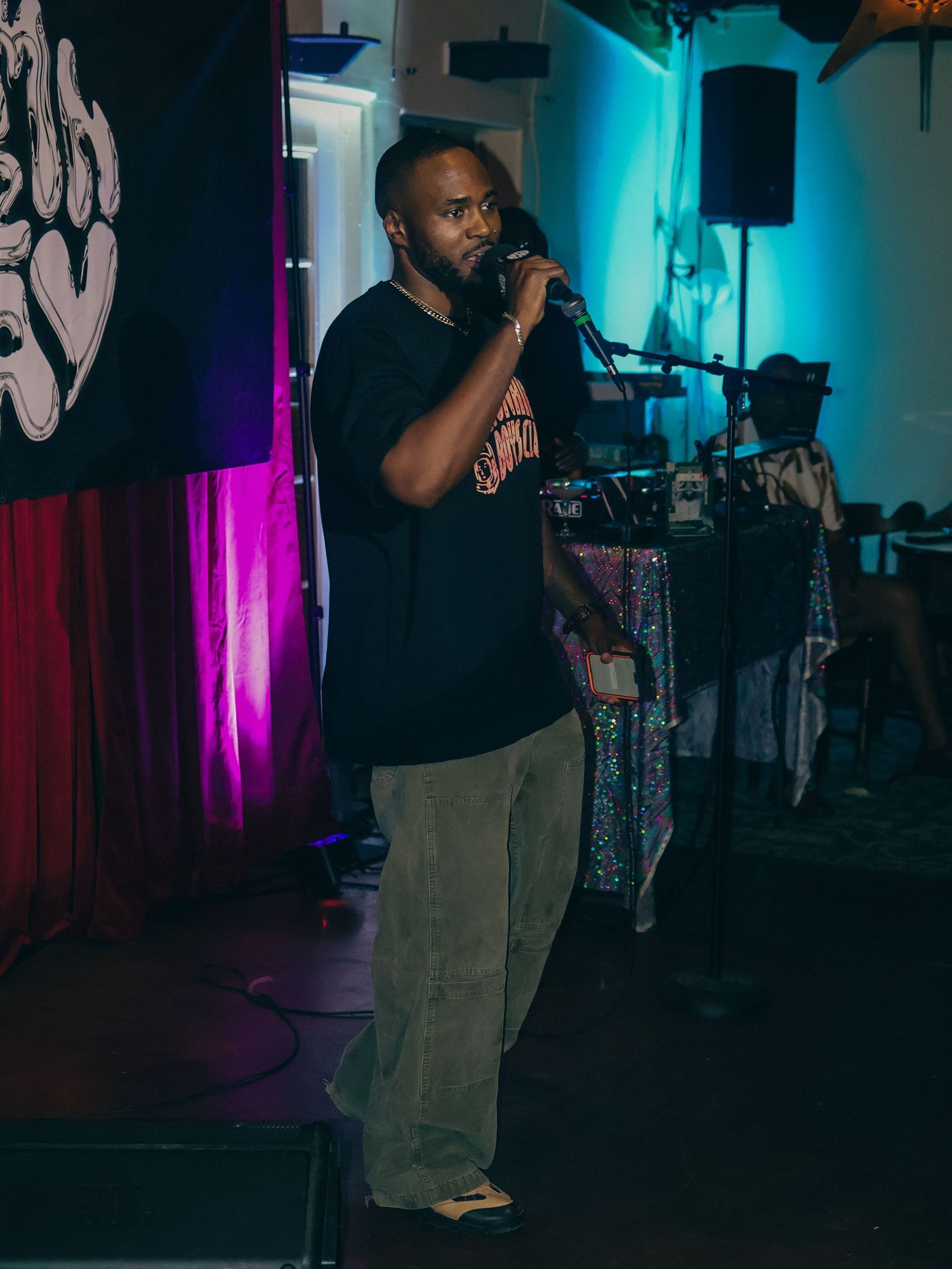 A performer on stage in dark lighting with colorful blue and purple accent lights in the background.