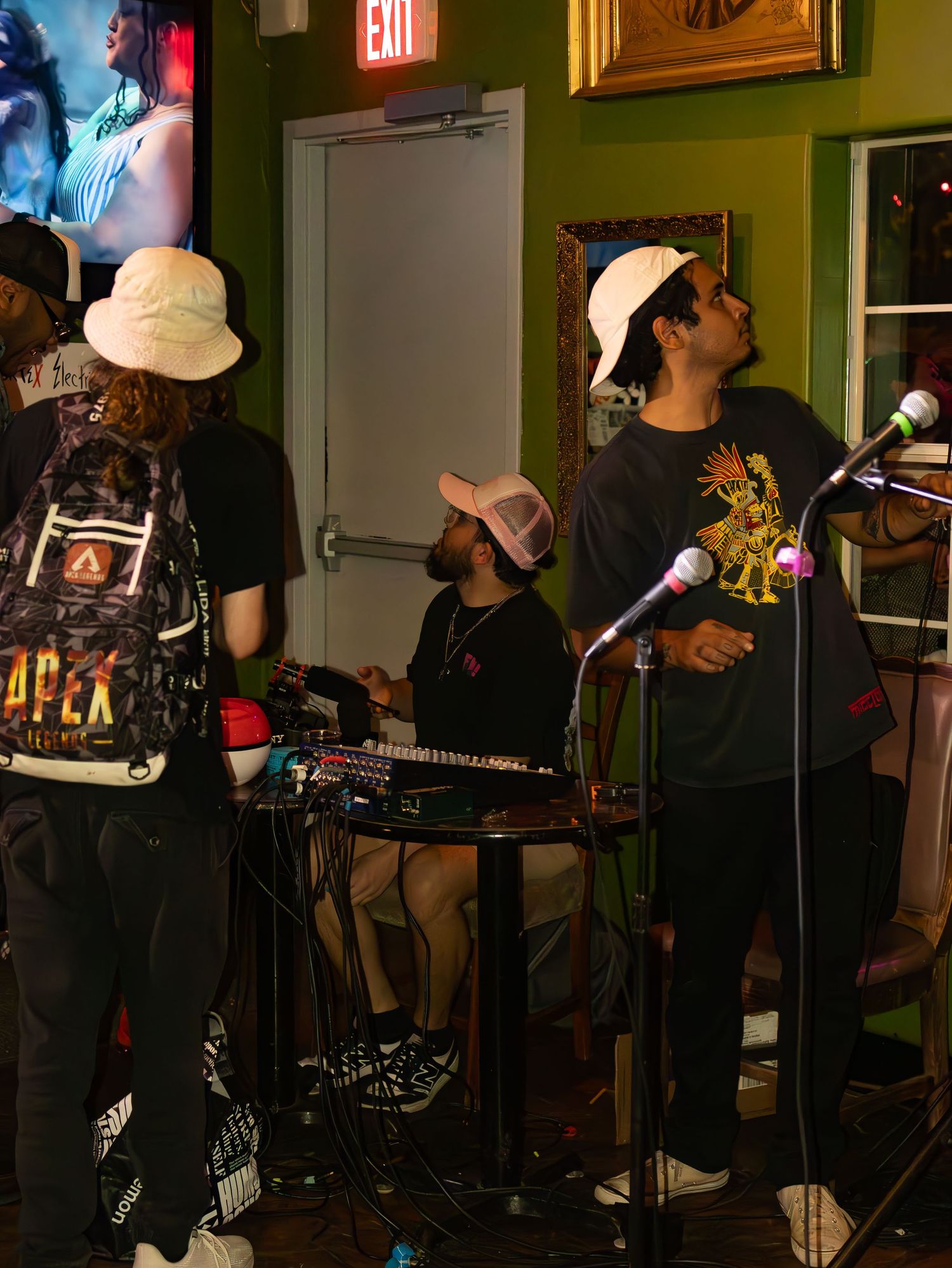 Band performing on dark stage with exit sign visible in background.