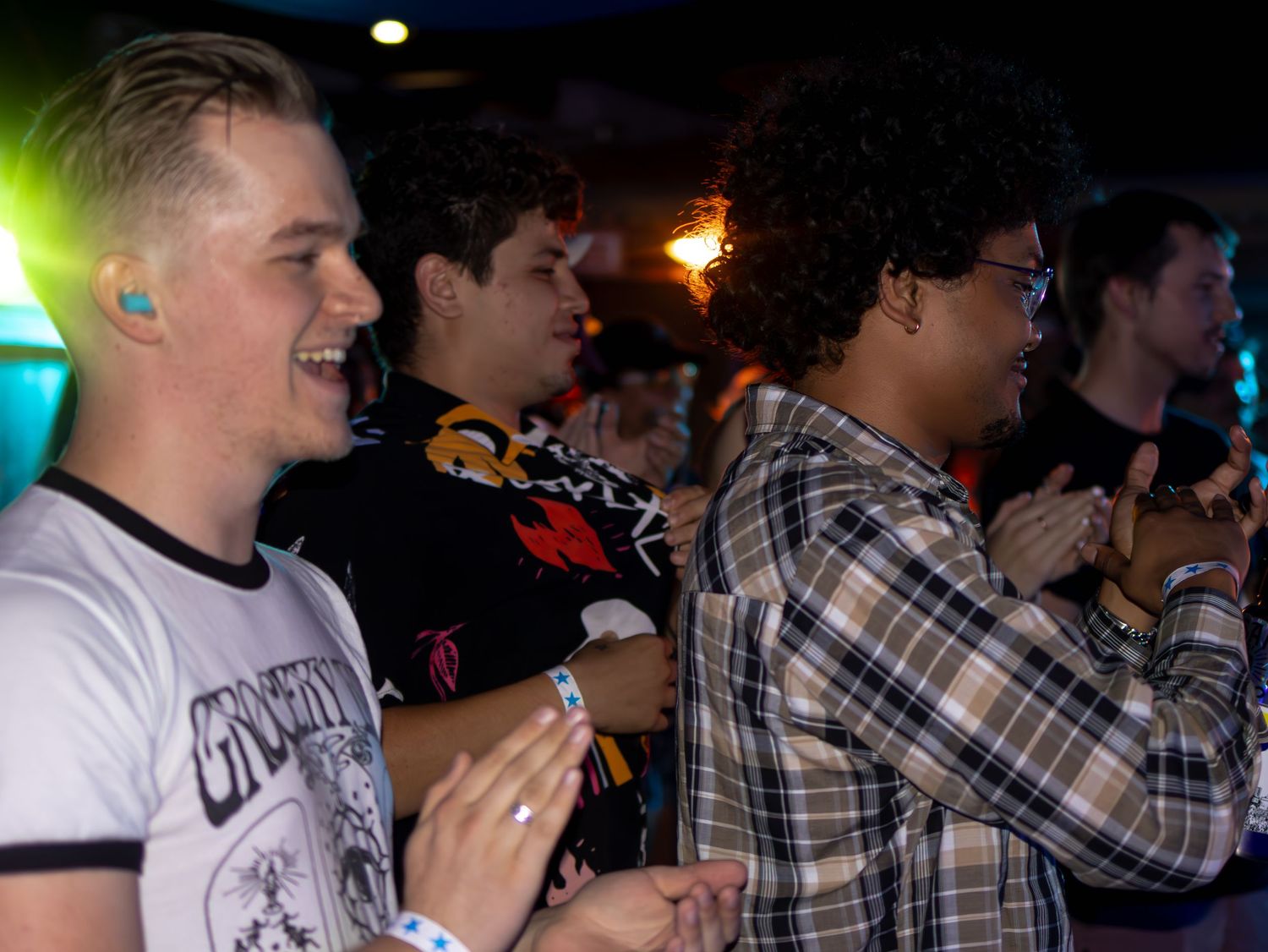 Crowd of people enjoying a live music performance in a dark venue with colorful lighting.