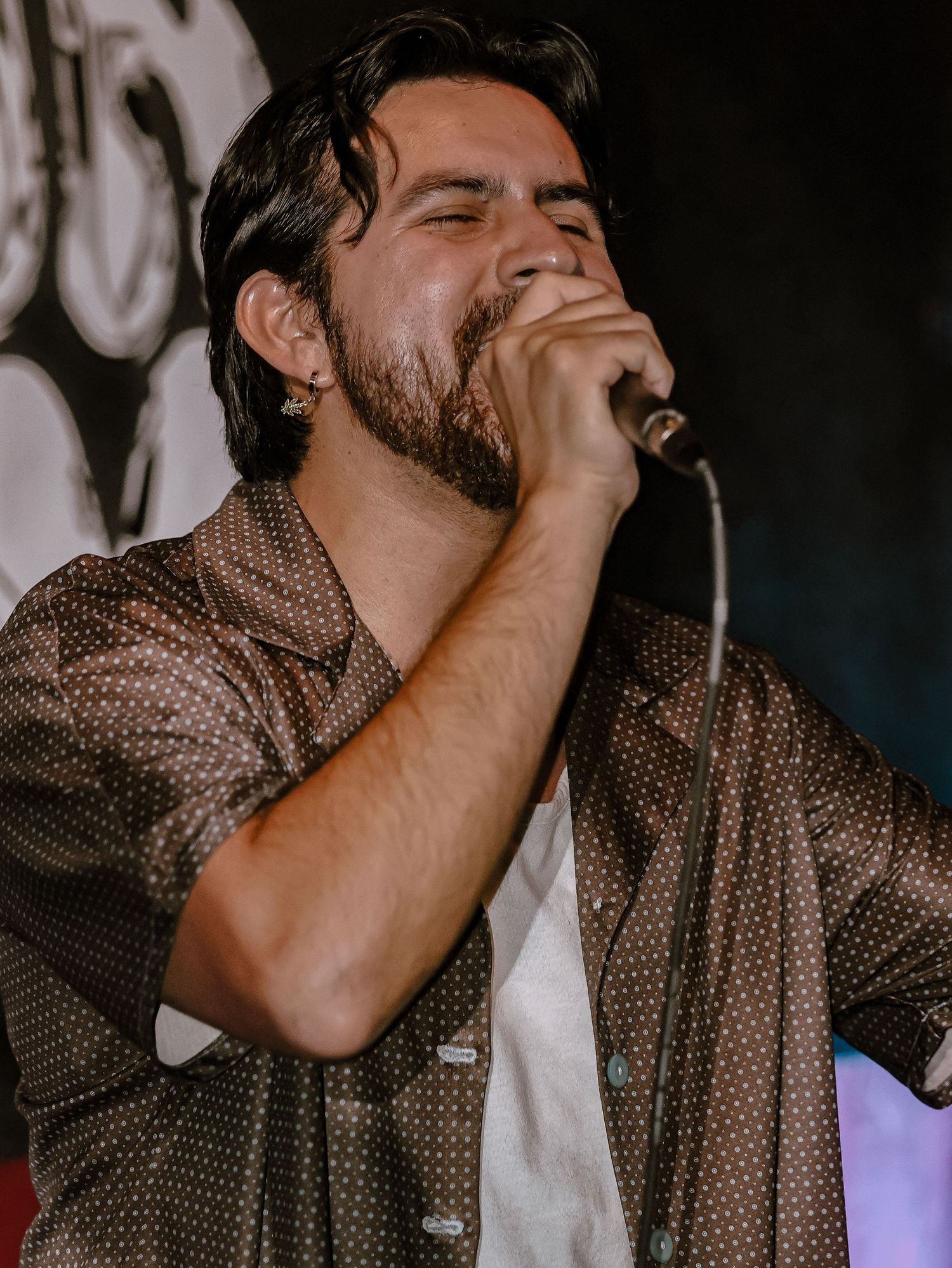 Singer performing passionately on stage in a brown polka dot shirt during a live concert.
