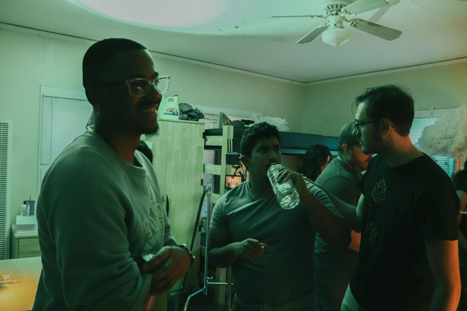 Film crew works under green-tinted lighting during an indoor production shoot.