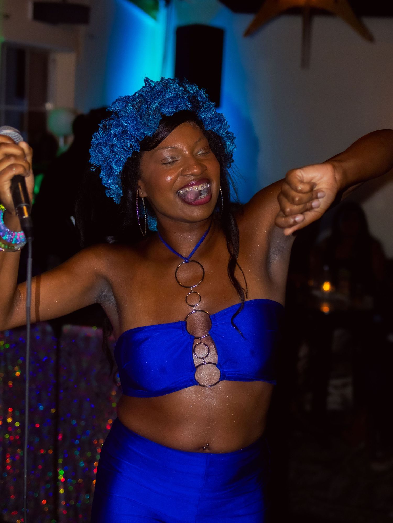 Singer in royal blue attire performs energetically under vibrant blue stage lighting.