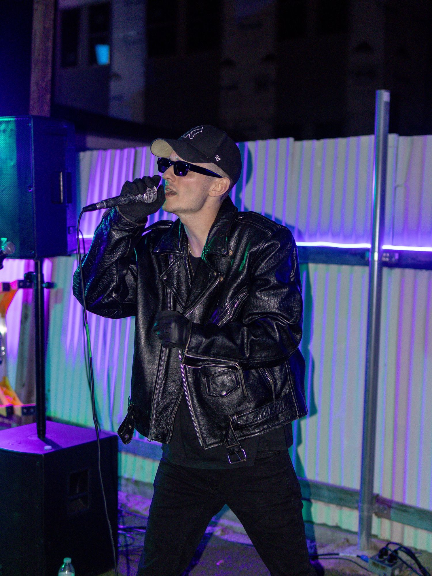 Artist in black ensemble performs on stage with blue and purple lighting effects.