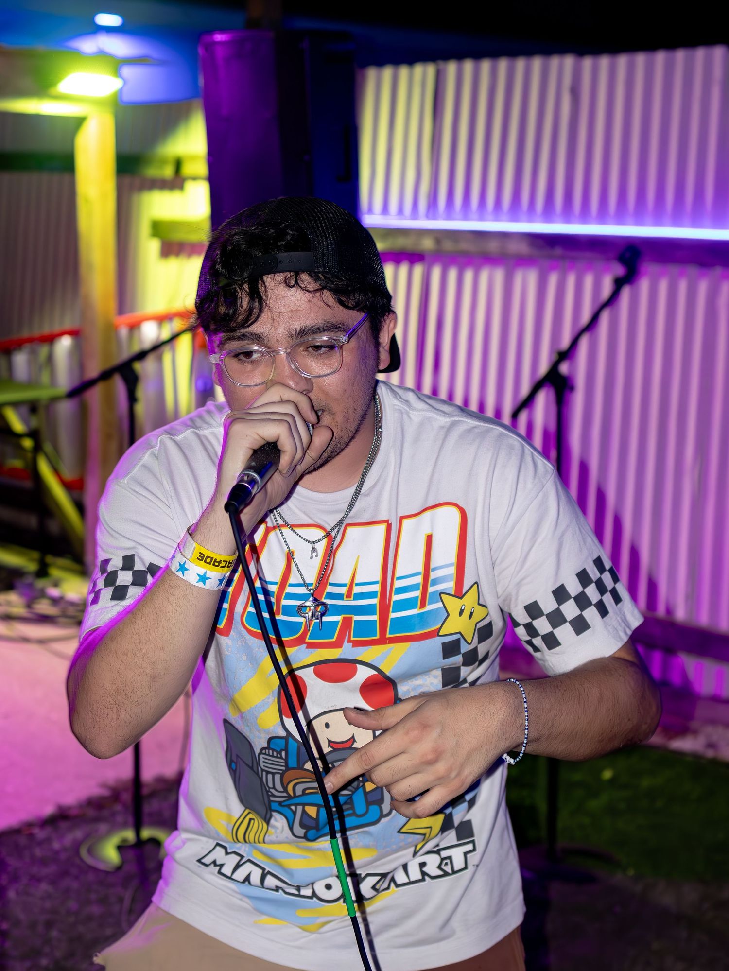 Performer in Nintendo-themed shirt singing passionately under mixed stage lighting.