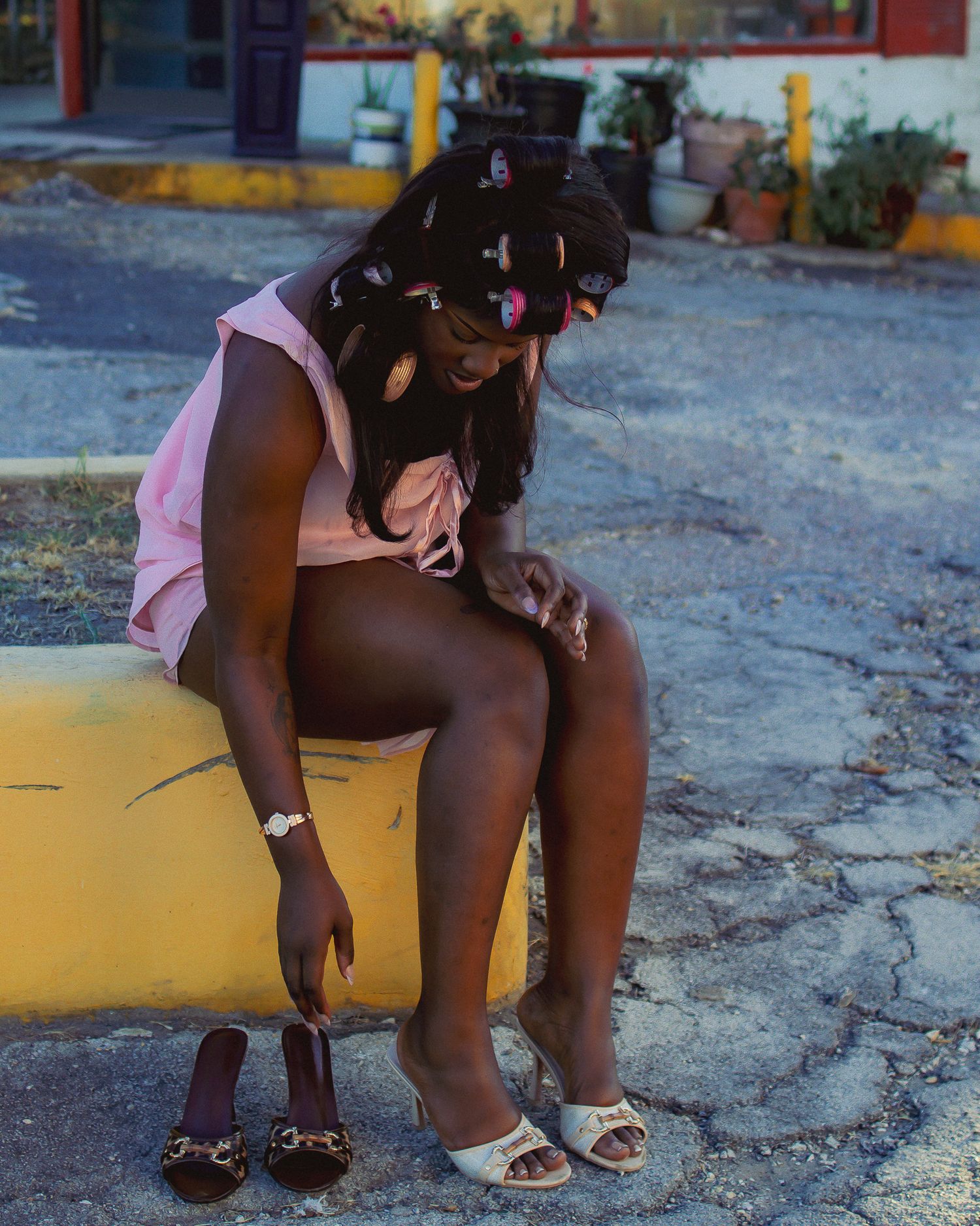 A person in pink clothing sits on a yellow curb in an outdoor setting.
