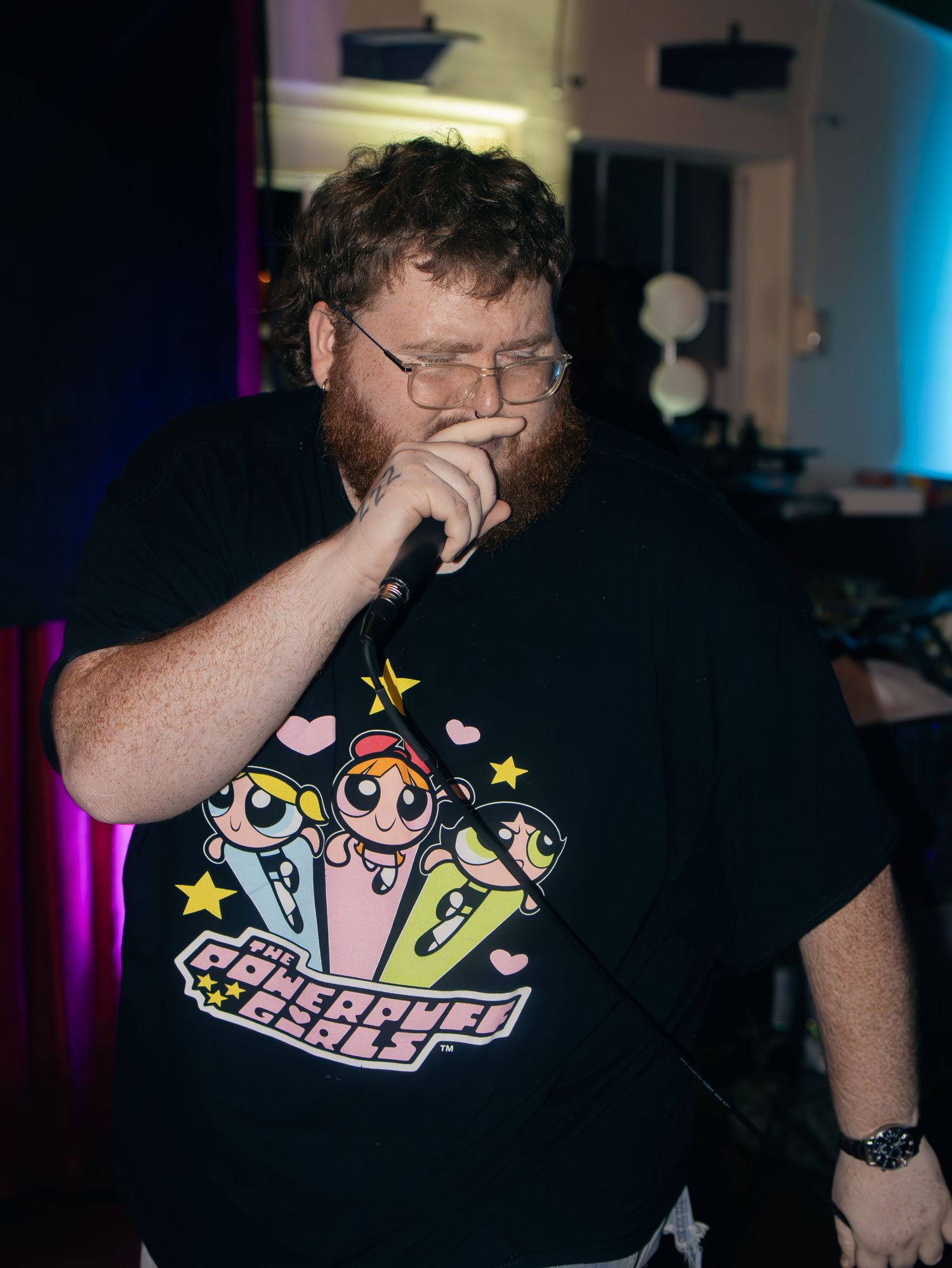 Performer in black t-shirt with animated character design singing during a live show.