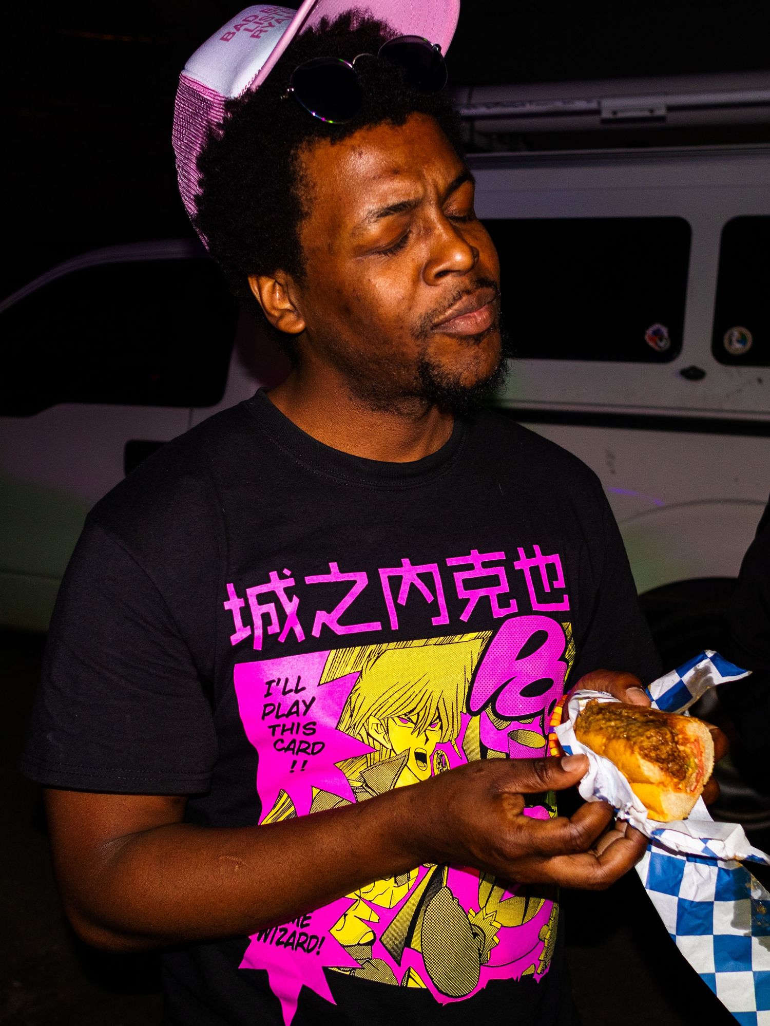Person wearing anime-style t-shirt enjoying food outdoors at night.