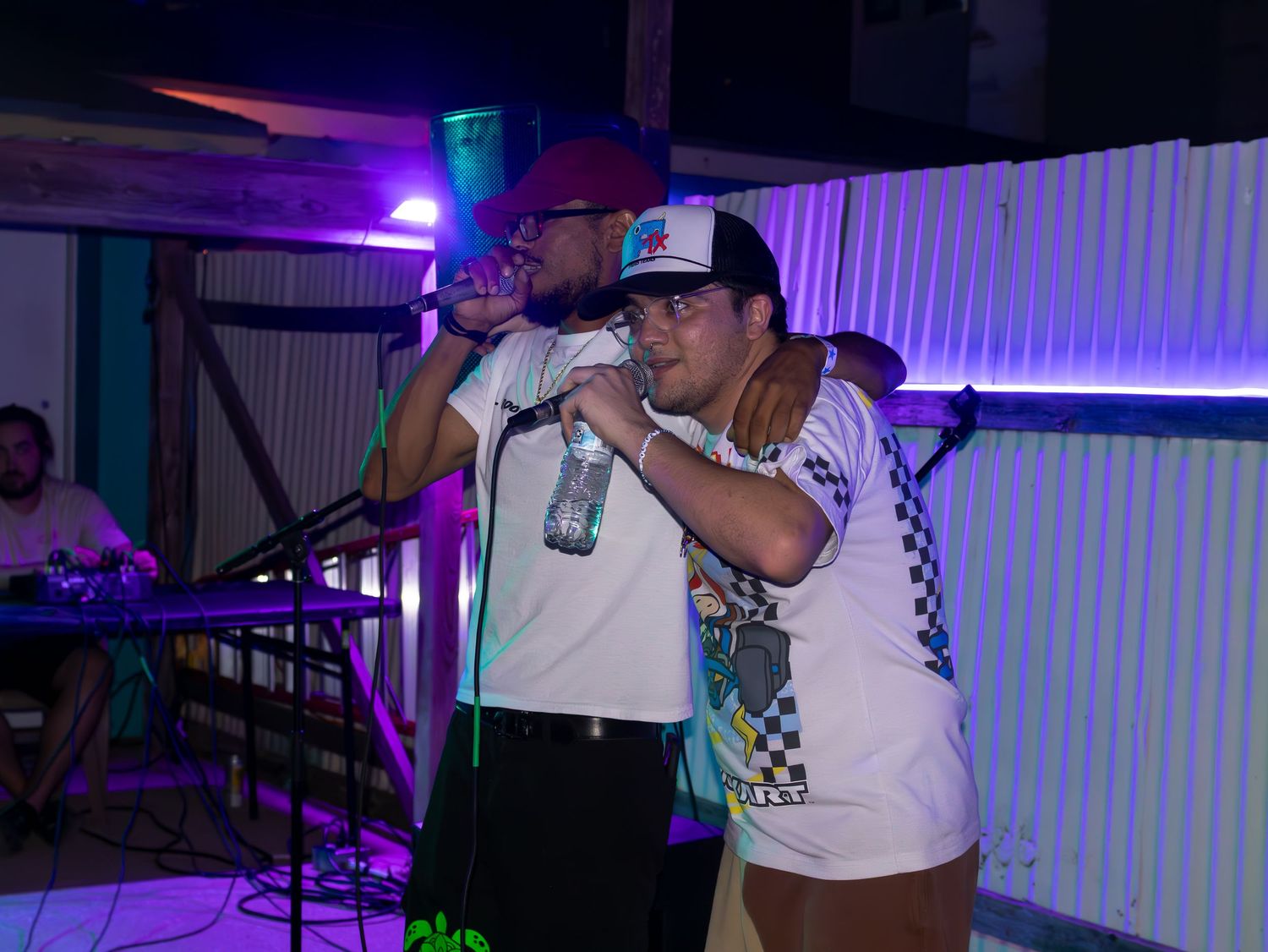 Musicians performing on stage with colorful lighting and white t-shirts with checkered patterns.