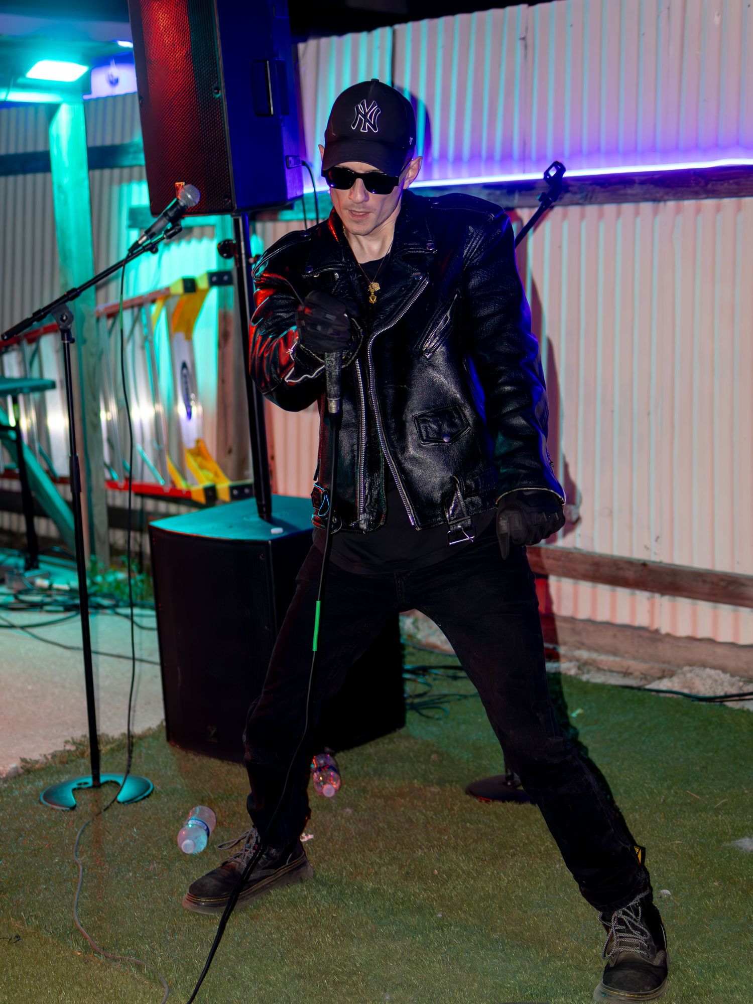 Stage performer in black leather strikes dynamic pose under blue and purple theatrical lighting.