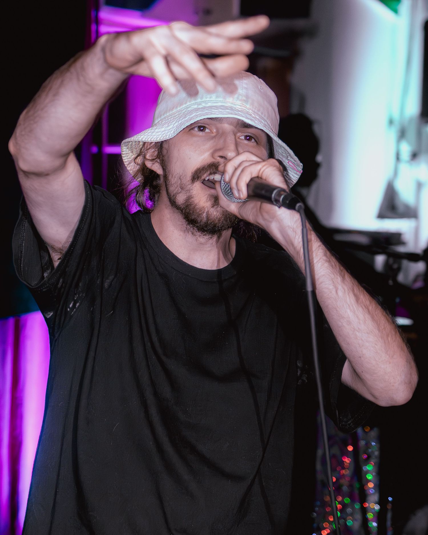 Performer in black shirt and white cap delivering passionate rap performance with dramatic gestures.