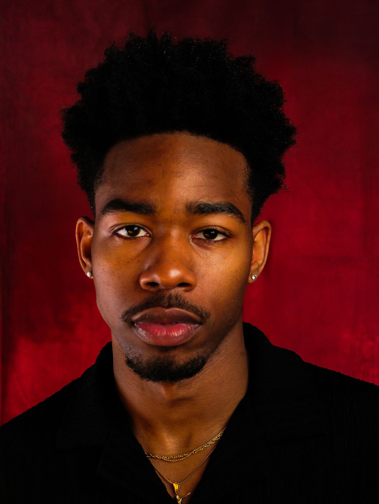 Studio portraits with red backdrop featuring black outfit and gold jewelry.
