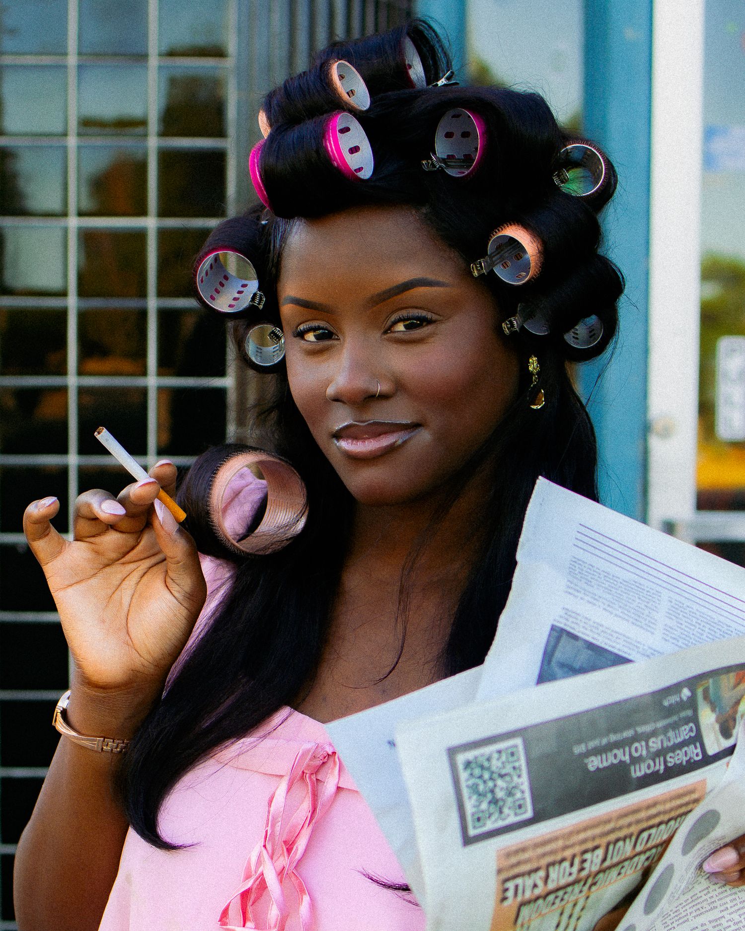 Elegant pose with styled hair in rollers while holding newspaper outdoors.