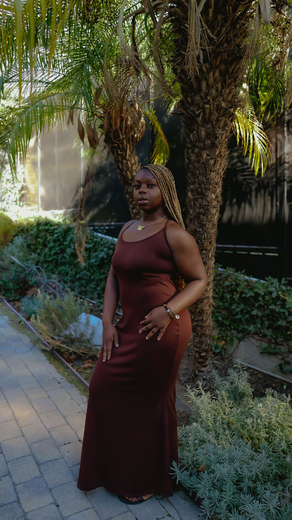 Full length portrait in brown dress among palm trees and stone pathway.