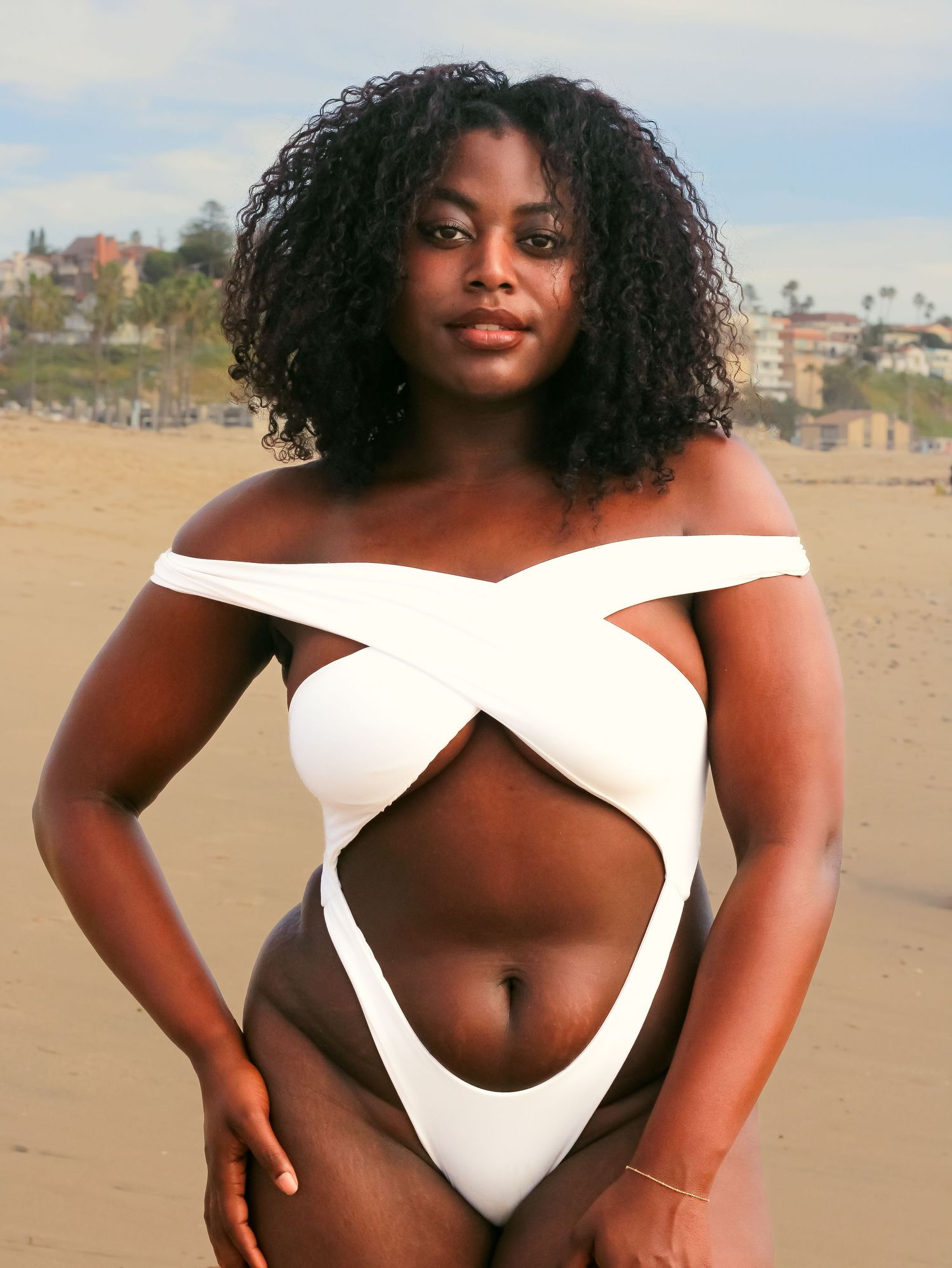 Fashion photo on beach showing model in white swimwear against sandy background.