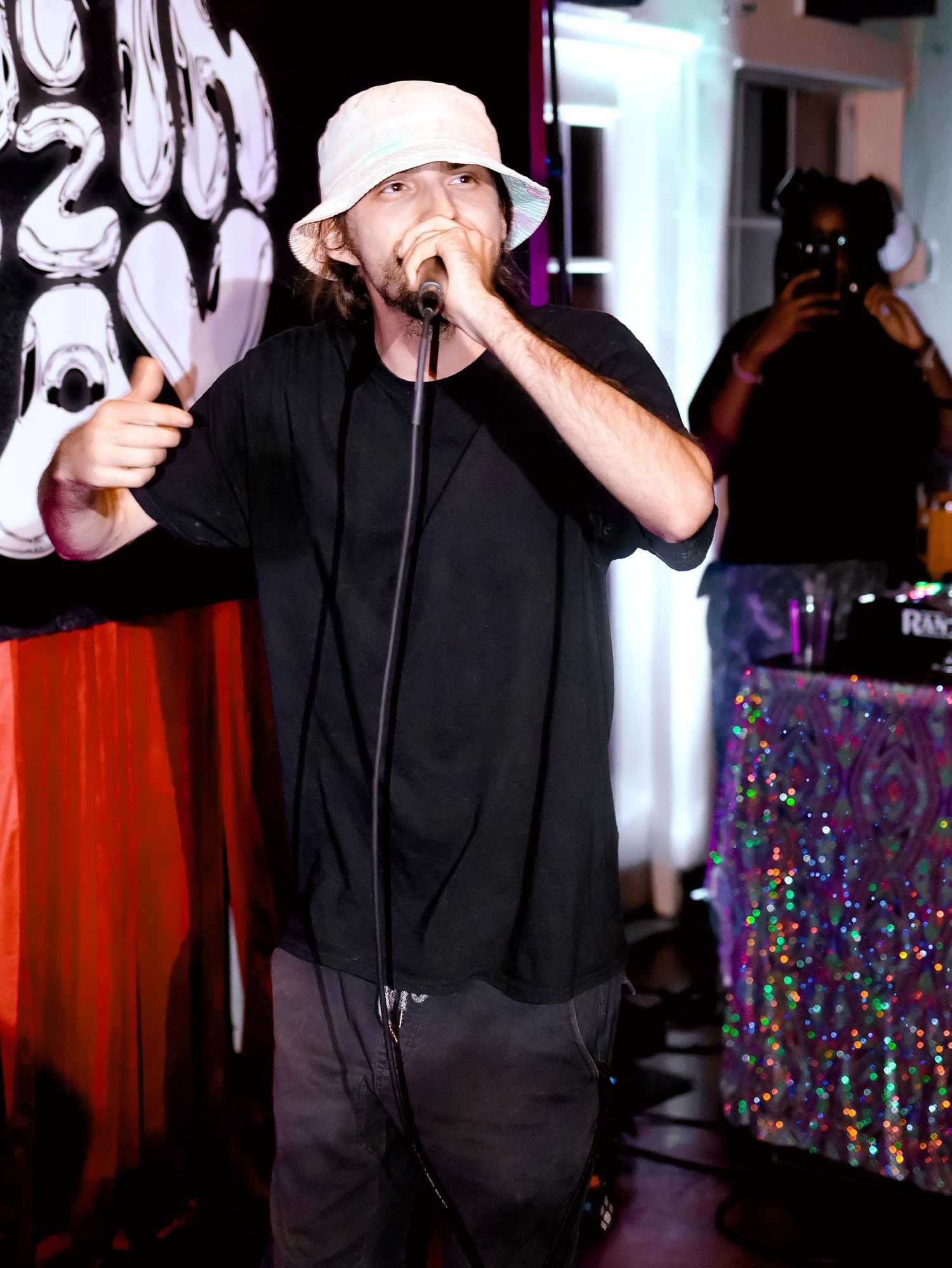 Artist performing on stage with microphone against backdrop of colorful lights and decorations.