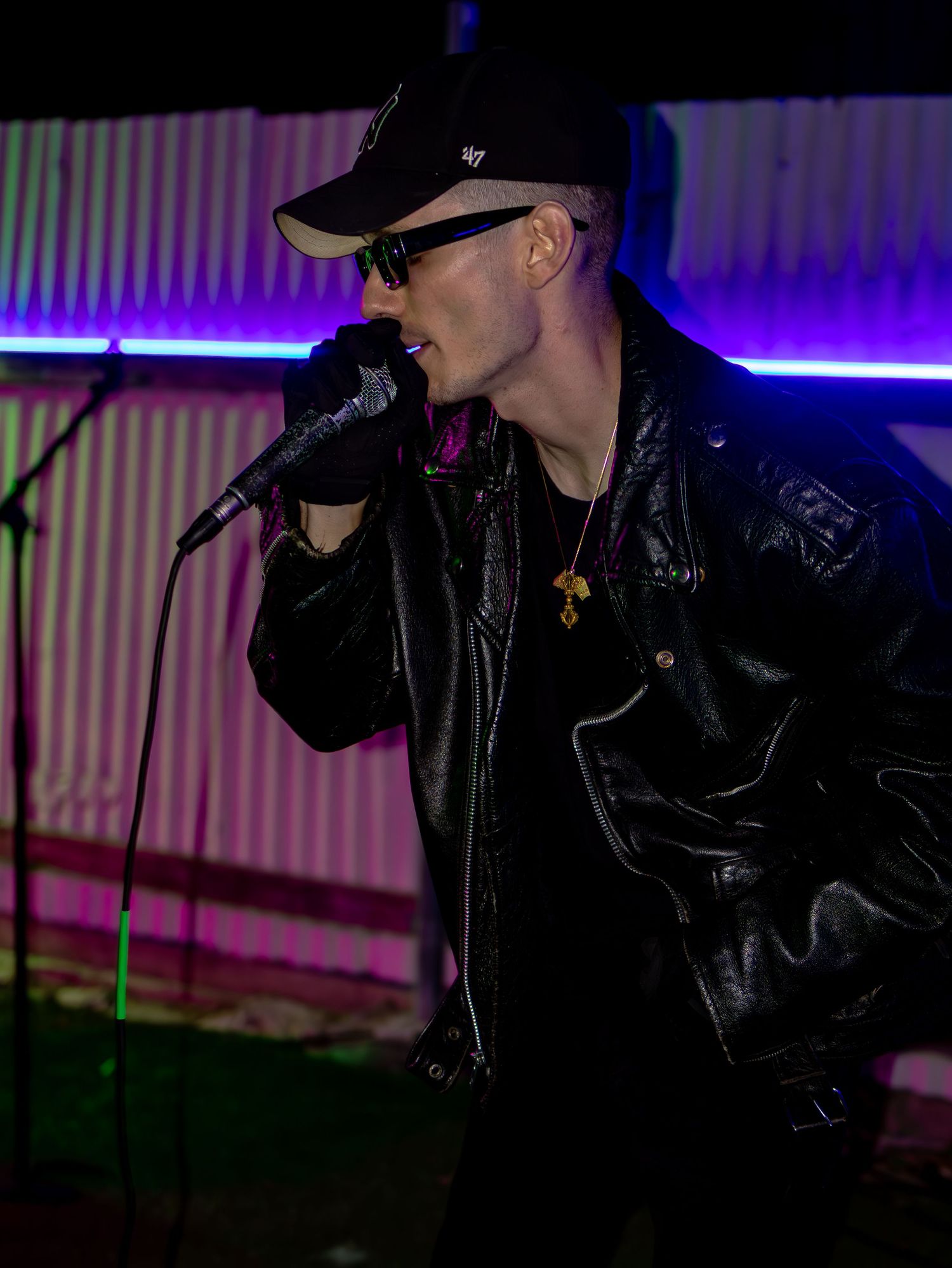 Vocalist in leather jacket and cap performing under dramatic purple and blue stage lights.