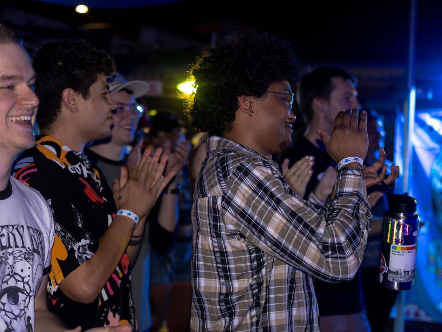 Crowd of concert attendees watching performance in dimly lit venue with blue lighting.