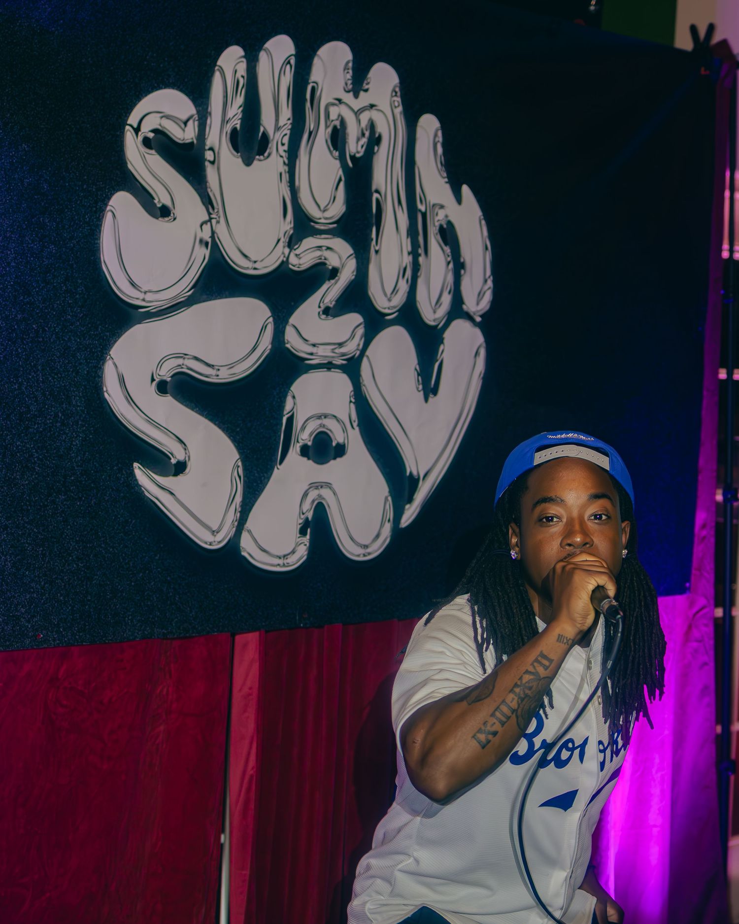 Artist performs with microphone against graffiti backdrop under blue and purple stage lighting.