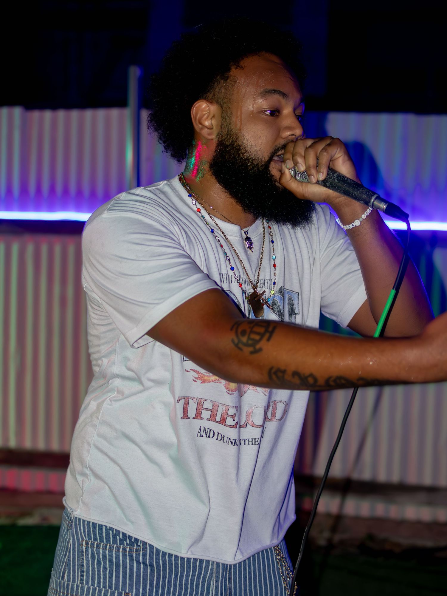 Artist in white t-shirt performing with dramatic gestures under colored stage lighting.