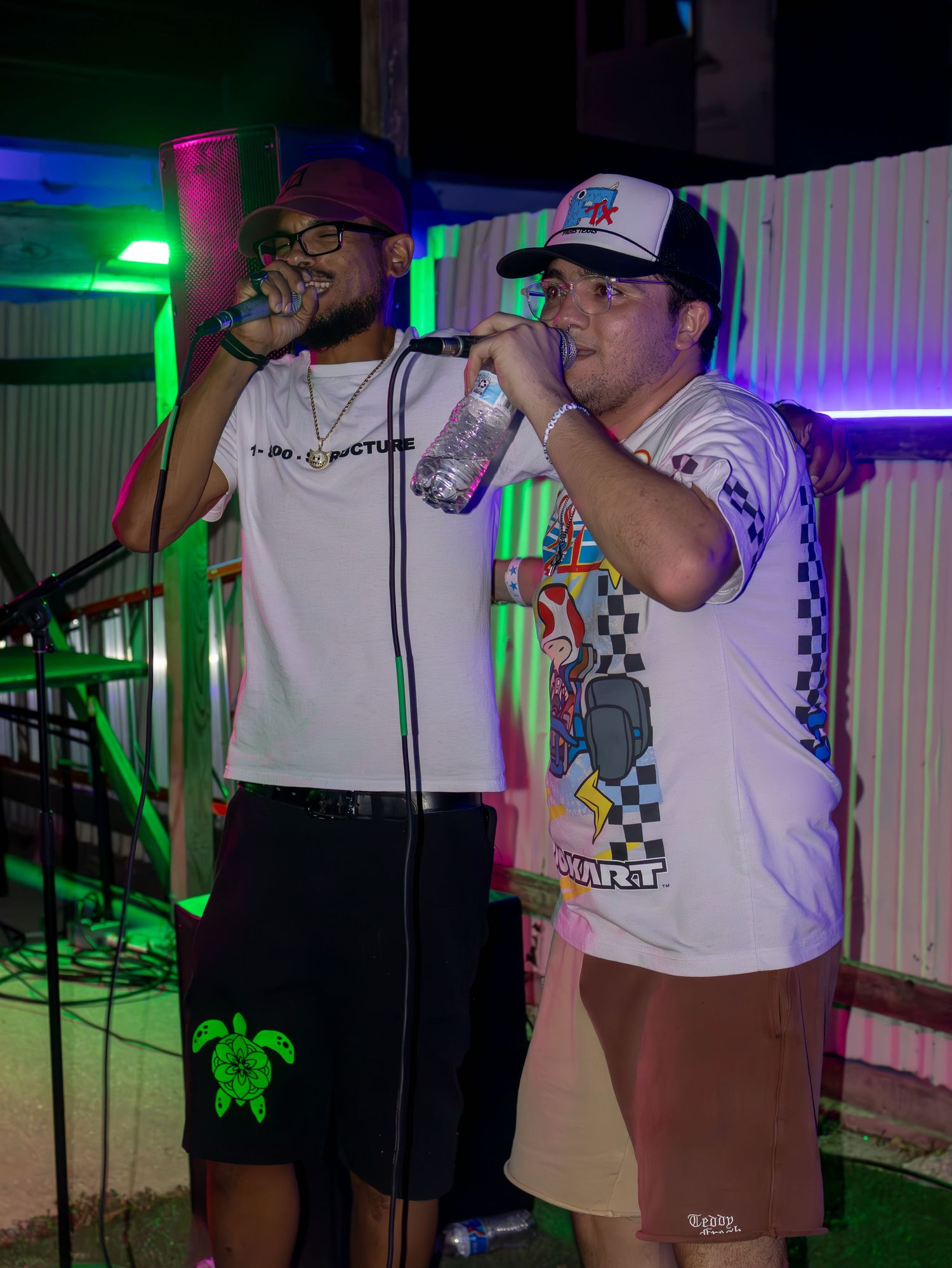 Performers on stage at a nightclub with colorful lighting and microphones in hand.