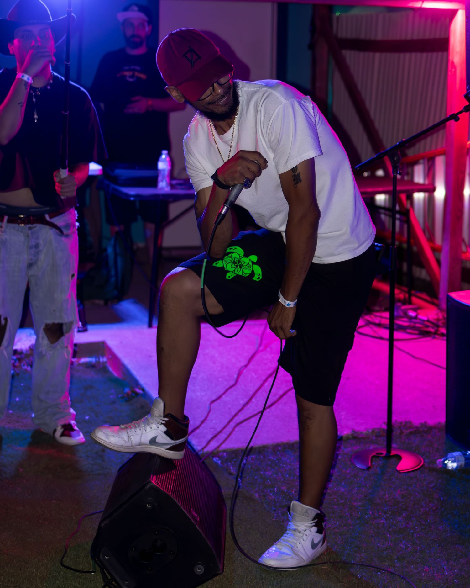 Concert performers on stage with pink and blue lighting effects in a nightclub setting.