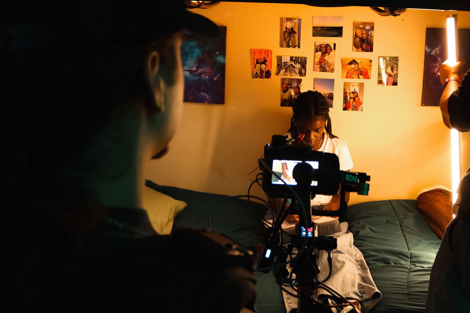 Camera operators work in warm-lit room with photos visible on wall behind them.