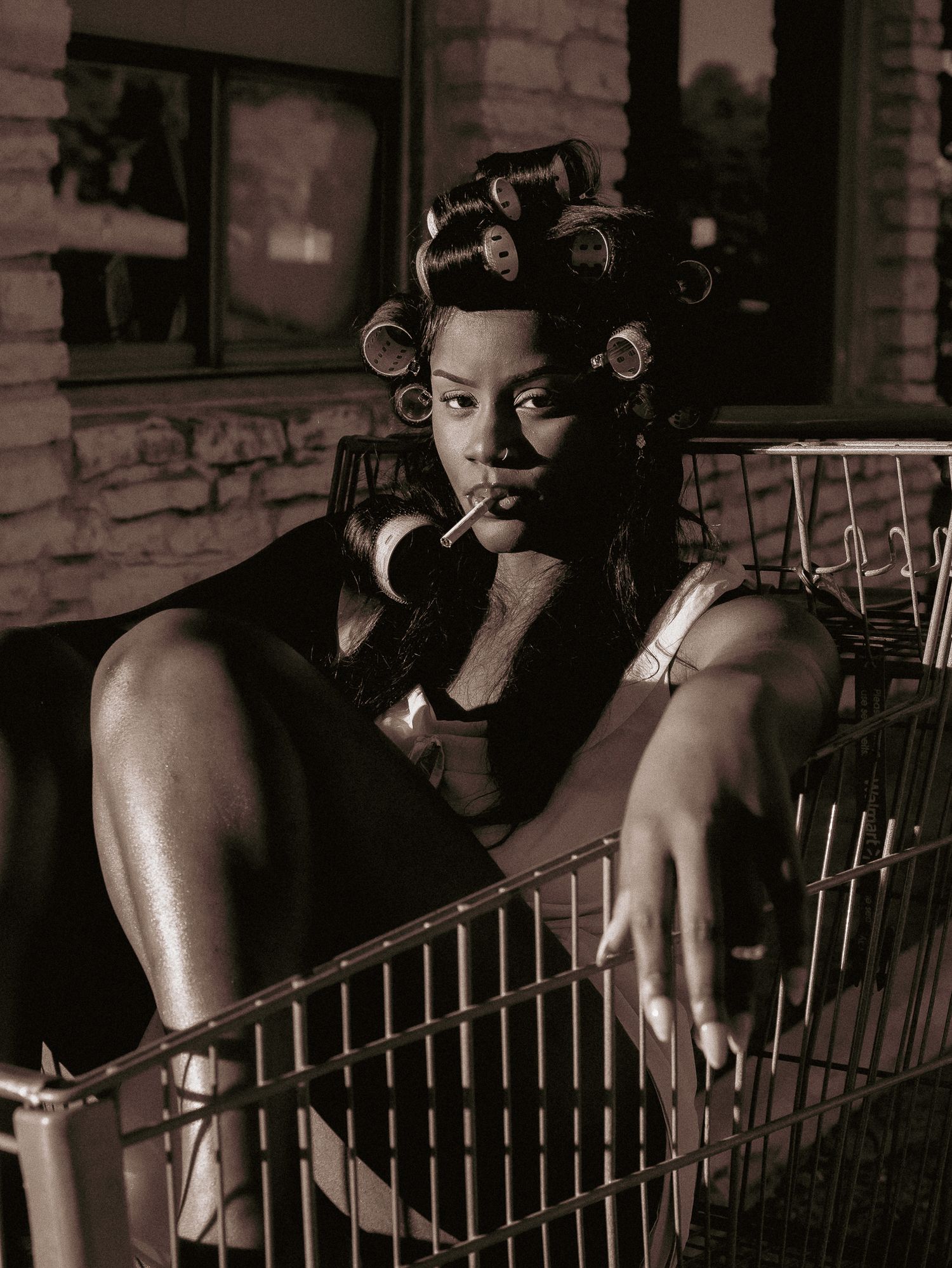 Vintage style photo of model lounging in shopping cart with hair in curlers.