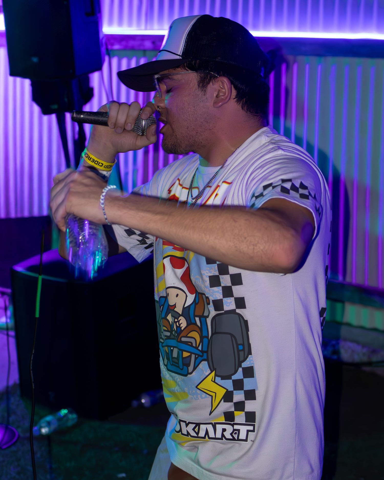 Concert performer in white gaming t-shirt with checkerboard pattern singing under purple lights.