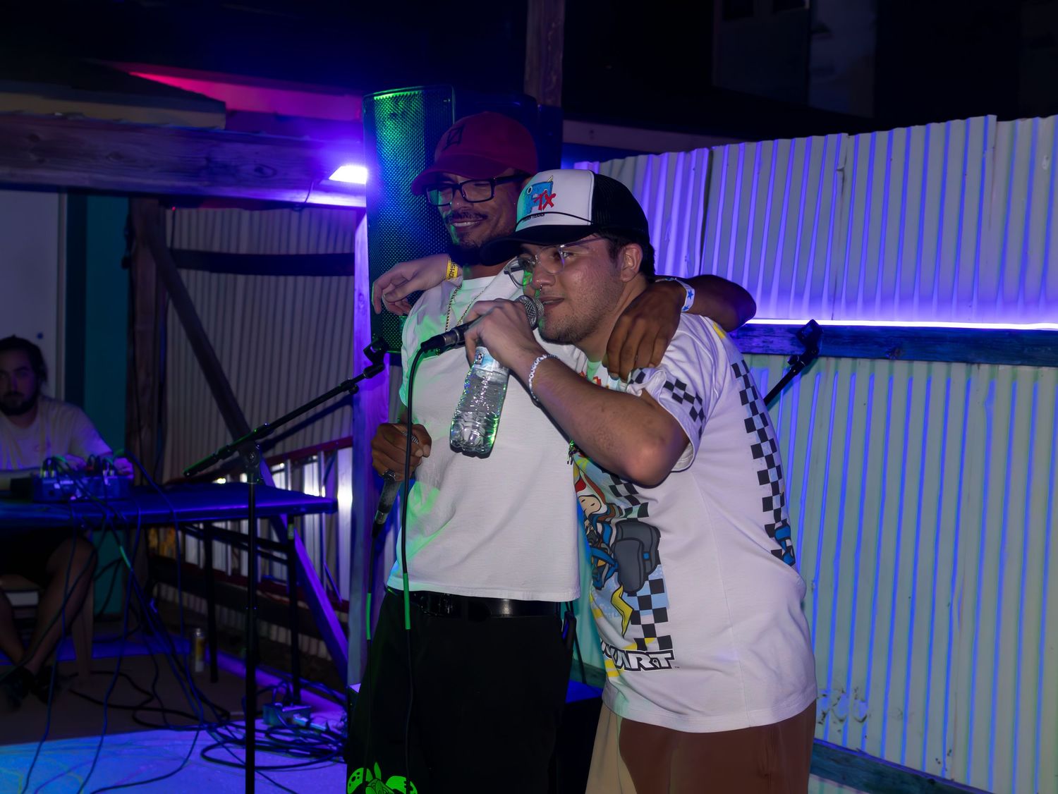 Performers singing on stage with neon lighting effects in a nightclub setting.