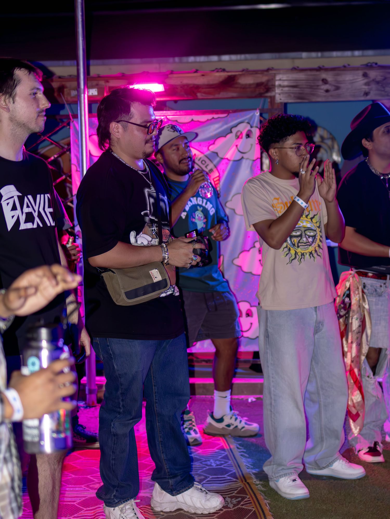 Concert audience standing together under pink and purple stage lighting at a nighttime event.