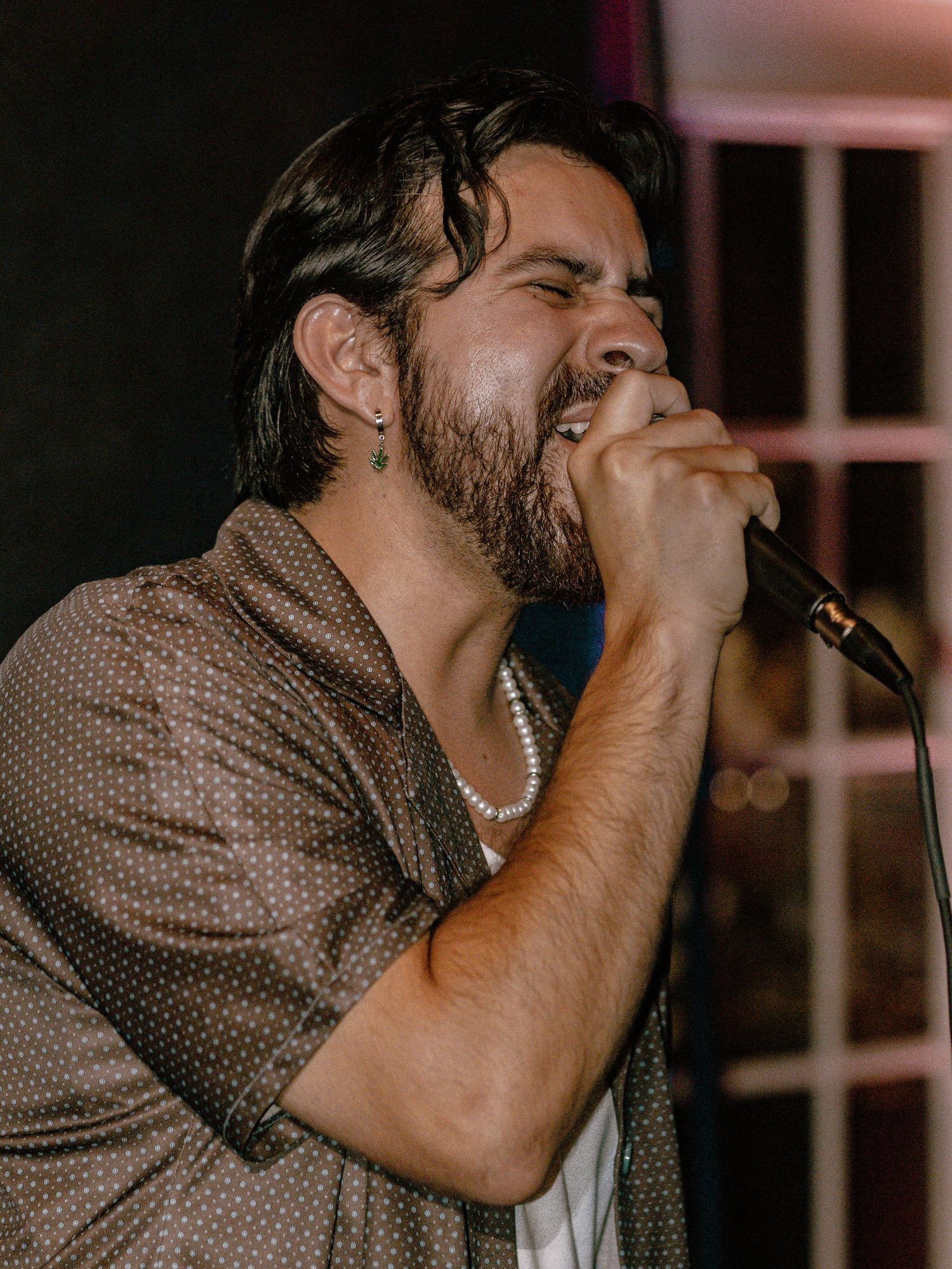 Side profile of vocalist performing with microphone in dark venue with dramatic lighting.