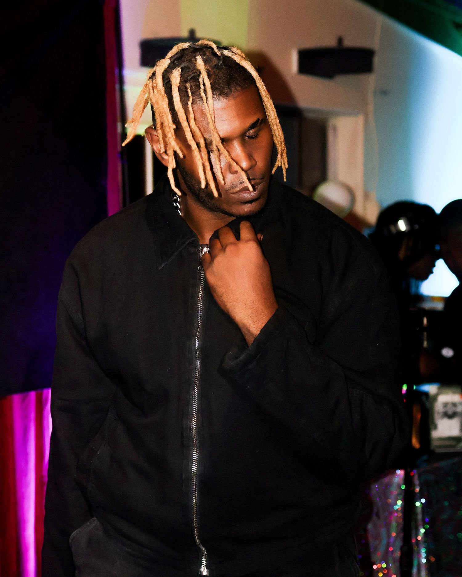 Hip hop artist performing on stage wearing black hoodie with blonde braided hairstyle.