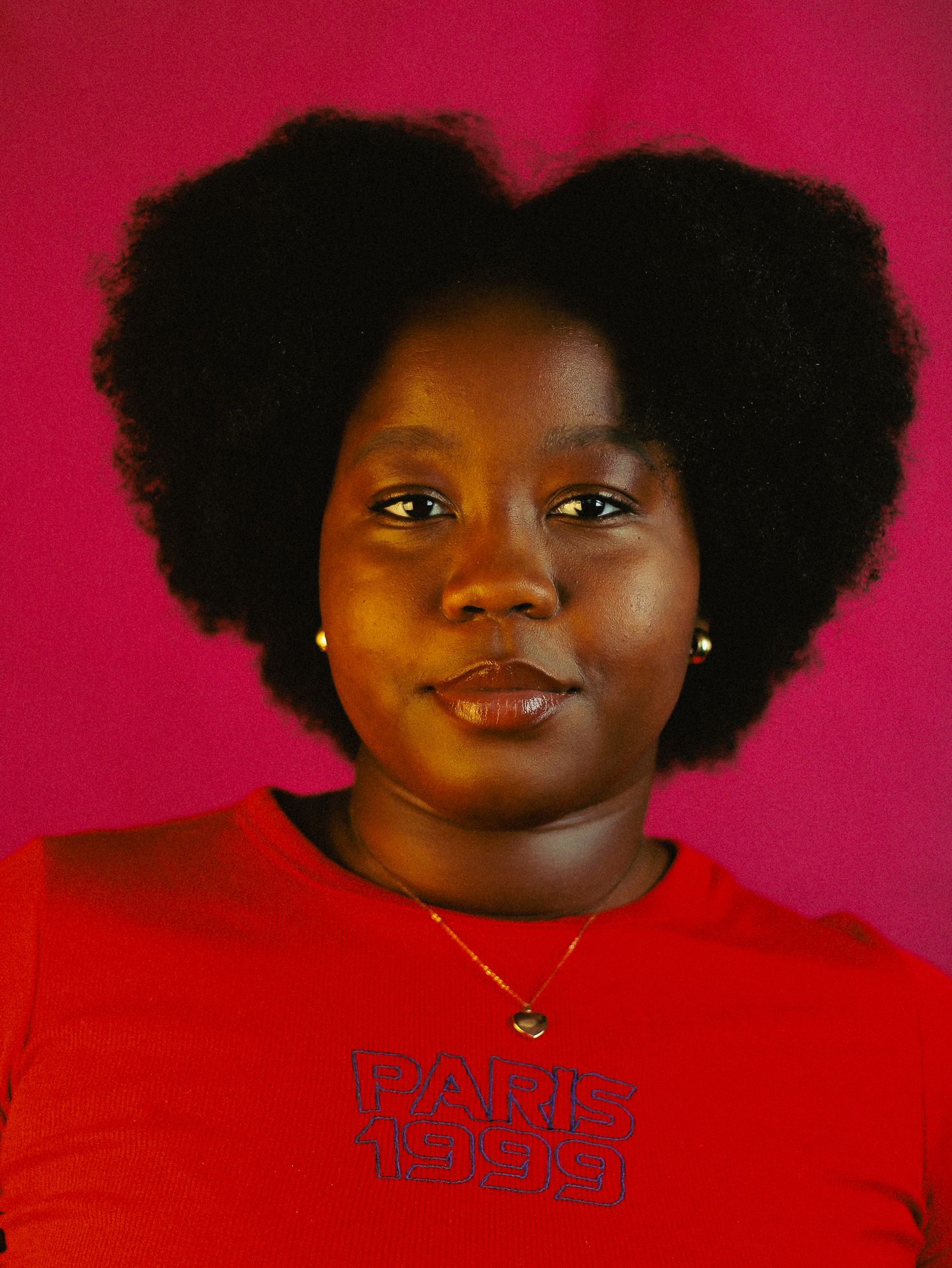 Young Black woman with large natural afro hair in red Paris tee against pink background.