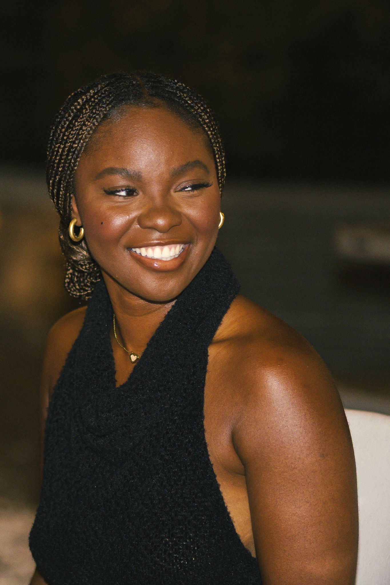 Person in black sleeveless top smiling warmly at a nighttime gathering.