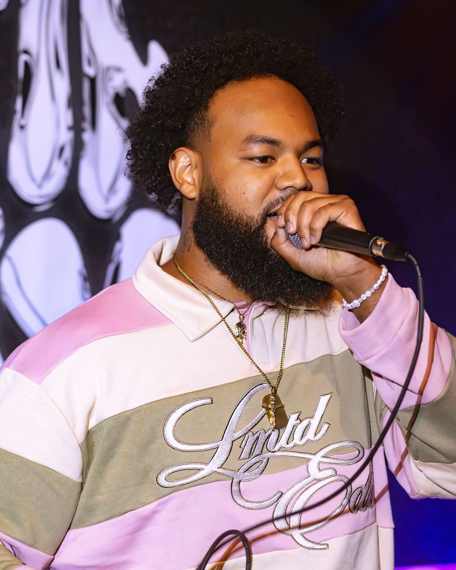 Singer wearing a two-tone jacket performing on stage with purple lighting effects.