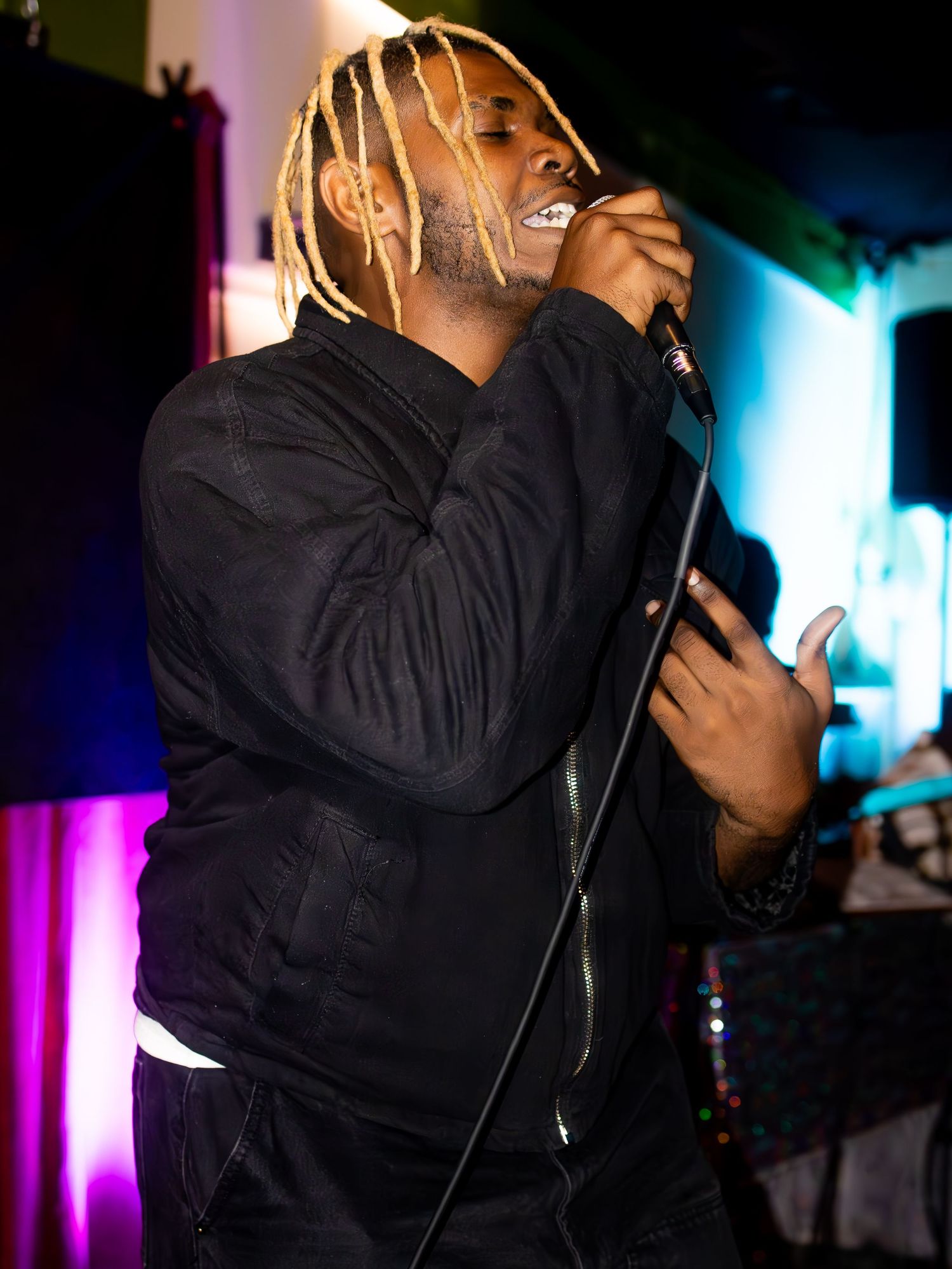 Energetic stage performance with artist in black jacket singing under vibrant lighting.
