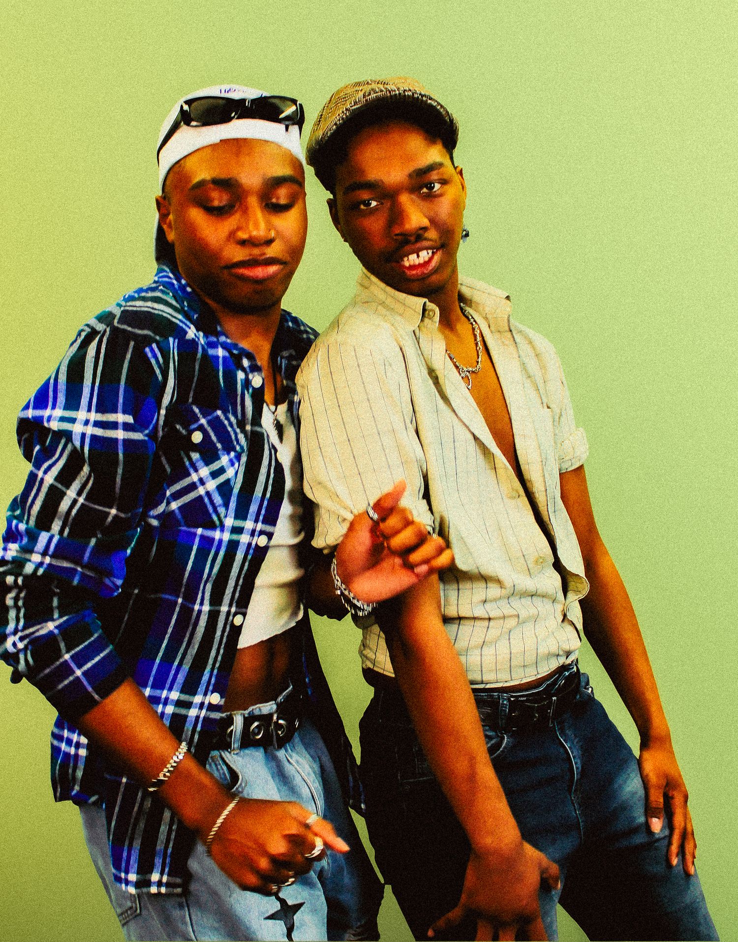 Two young Black friends in vintage 90s-inspired outfits pose together against a muted green background.