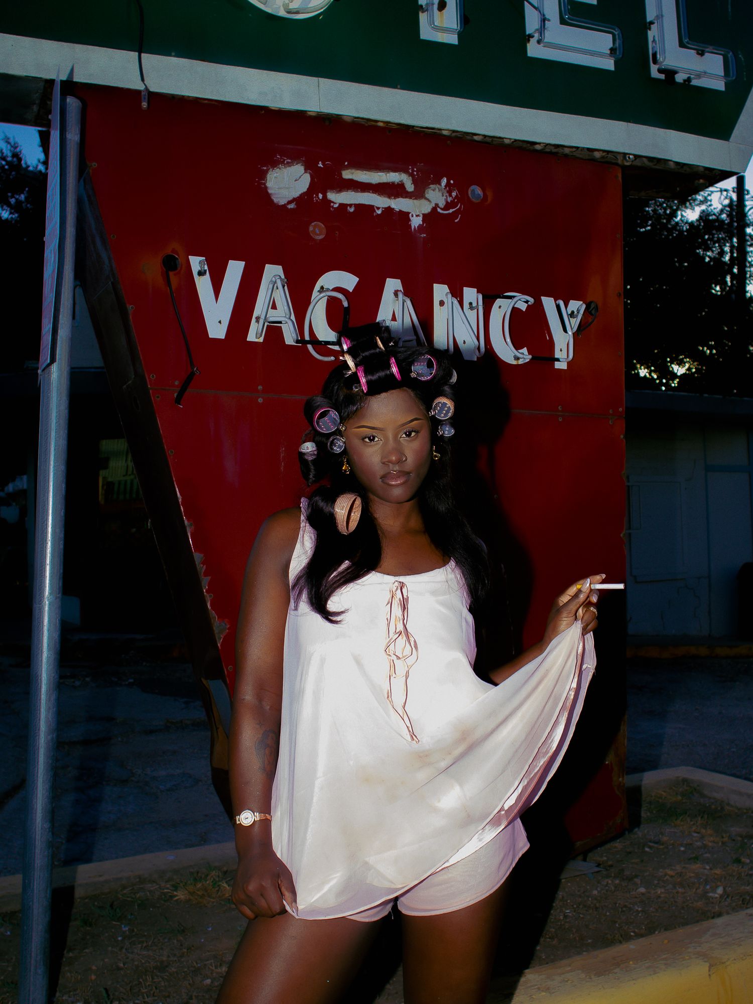 A fashion photoshoot in front of a motel vacancy sign with pink lighting and retro styling.